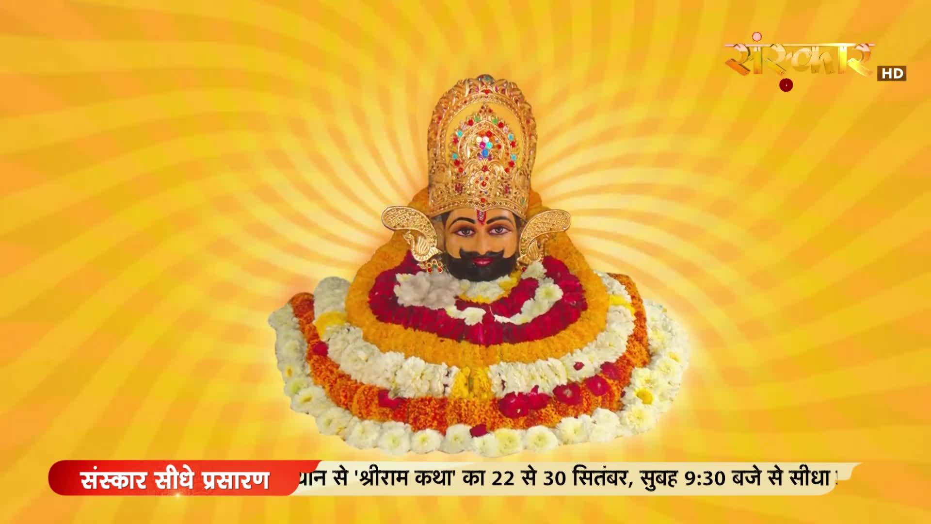 A deity is centered, adorned with a jeweled crown and garlands of flowers. The Sanskar TV logo and text about "Shriram Katha" broadcast details are at the top and bottom of the screen.
