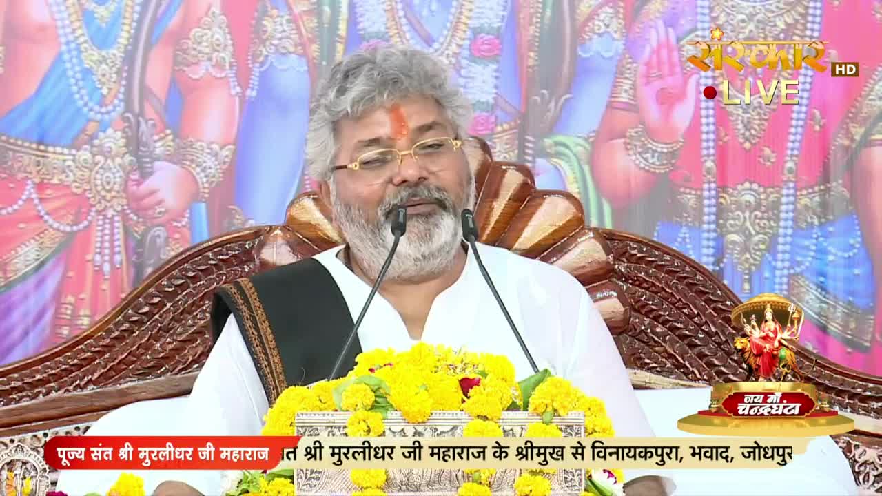A man with a white beard and glasses speaks into two microphones, his words likely broadcast on Sanskar TV. A banner at the bottom identifies him as Shri Murlidhar Ji Maharaj, speaking from Vinayakpura, India.
