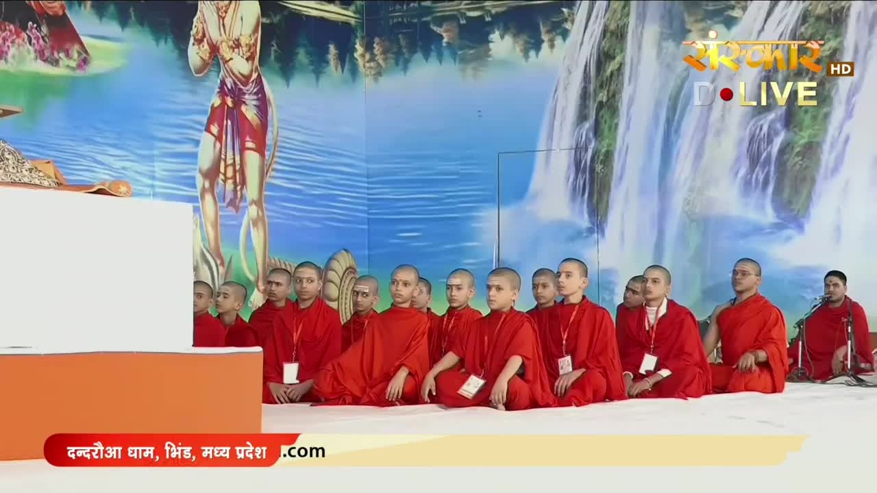 A group of men in red robes sit cross-legged, facing forward. The Sanskar TV logo is visible, and the scene is likely being broadcast live from India.
A group of men in red robes sit cross-legged, facing forward. The Sanskar TV logo is visible, and the scene is likely being broadcast live from India.