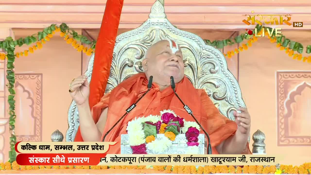 A man in an orange robe sits on an ornate chair, speaking into two microphones. The scene, broadcast live on Sanskar TV, is taking place in India, with text on the screen identifying the location as Kalki Dham, Sambhal, Uttar Pradesh.
A man in an orange robe sits on an ornate chair, speaking into two microphones. The scene, broadcast live on Sanskar TV, is taking place in India, with text on the screen identifying the location as Kalki Dham, Sambhal, Uttar Pradesh.