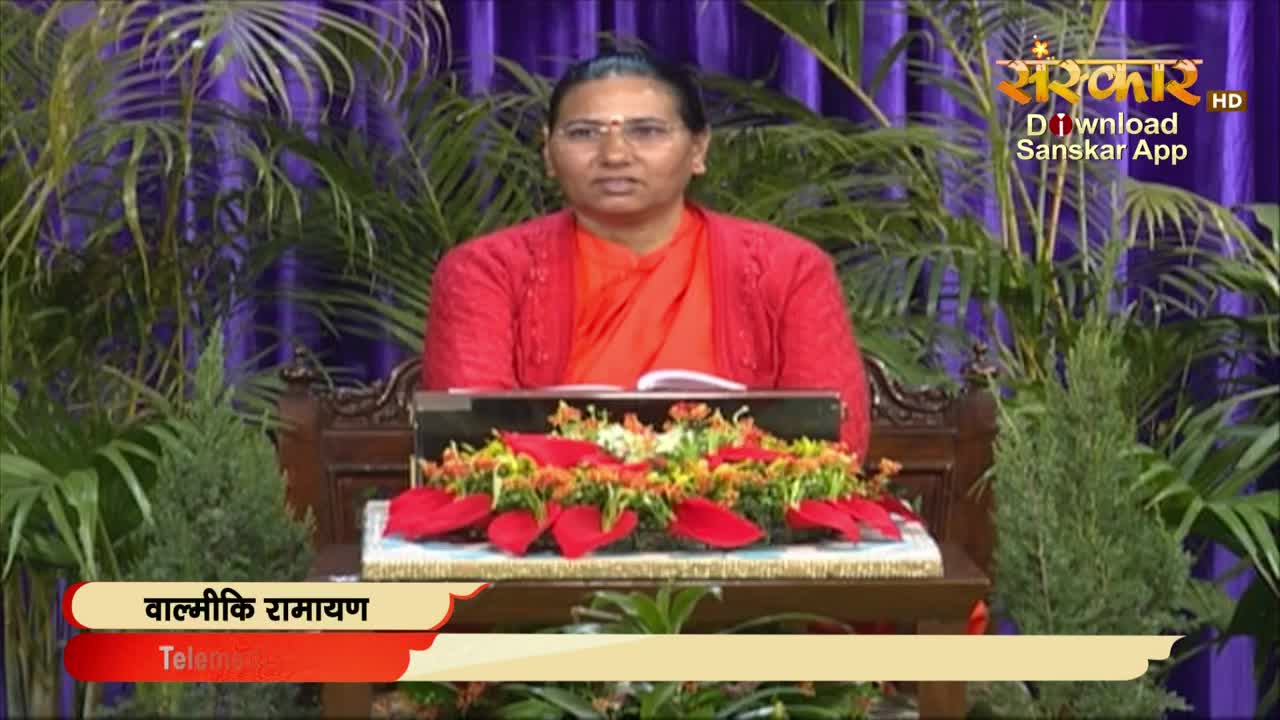 On Sanskar TV, a woman in a red sweater sits behind a small desk, speaking directly into the camera. The set is decorated with plants and a floral arrangement, with a banner for "Valmiki Ramayan" visible at the bottom.
On Sanskar TV, a woman in a red sweater sits behind a small desk, speaking directly into the camera. The set is decorated with plants and a floral arrangement, with a banner for "Valmiki Ramayan" visible at the bottom.