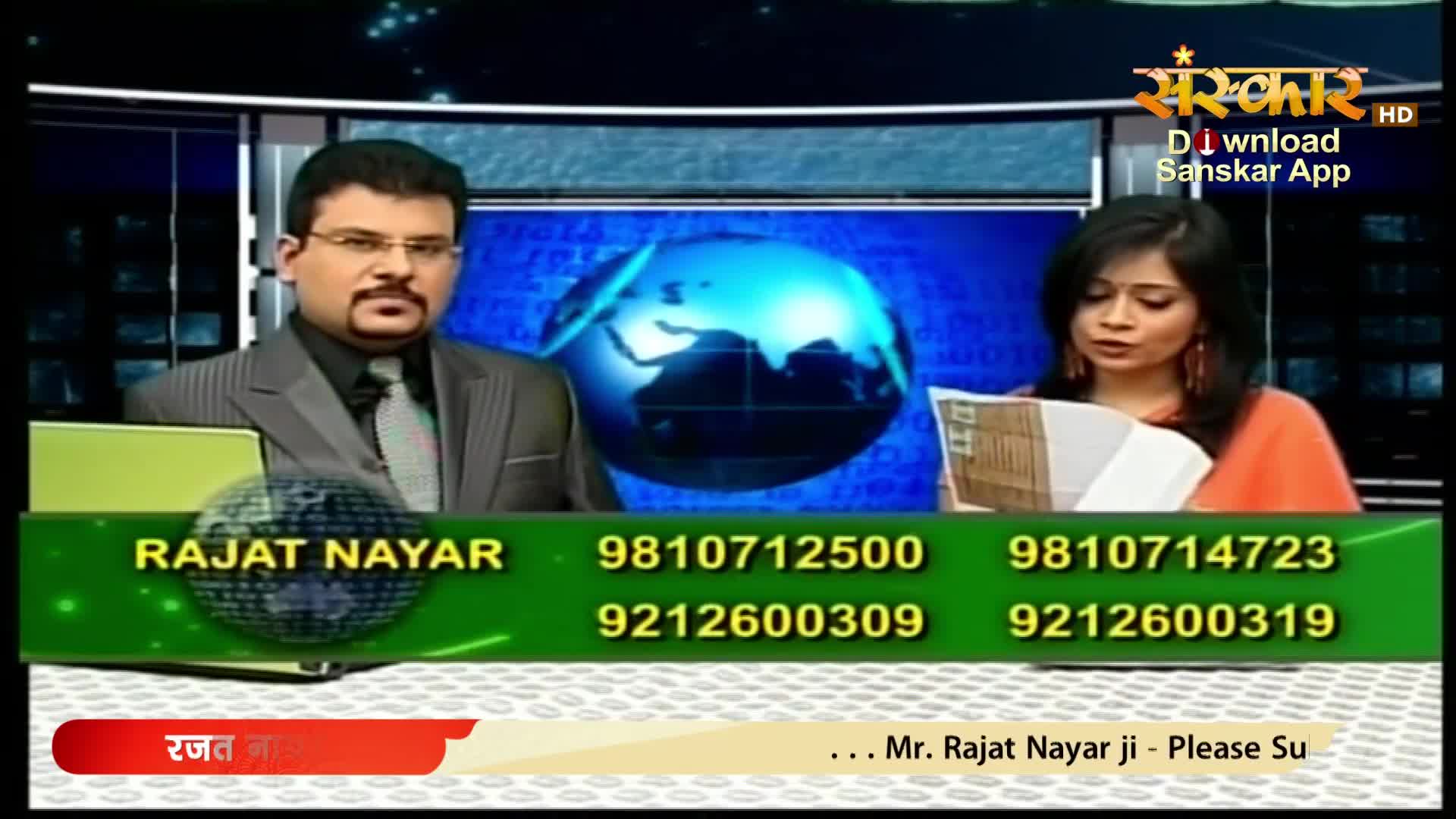 A man in a suit and tie looks directly ahead, while a woman beside him reads from a stack of papers. The Sanskar TV logo is visible in the upper right corner.