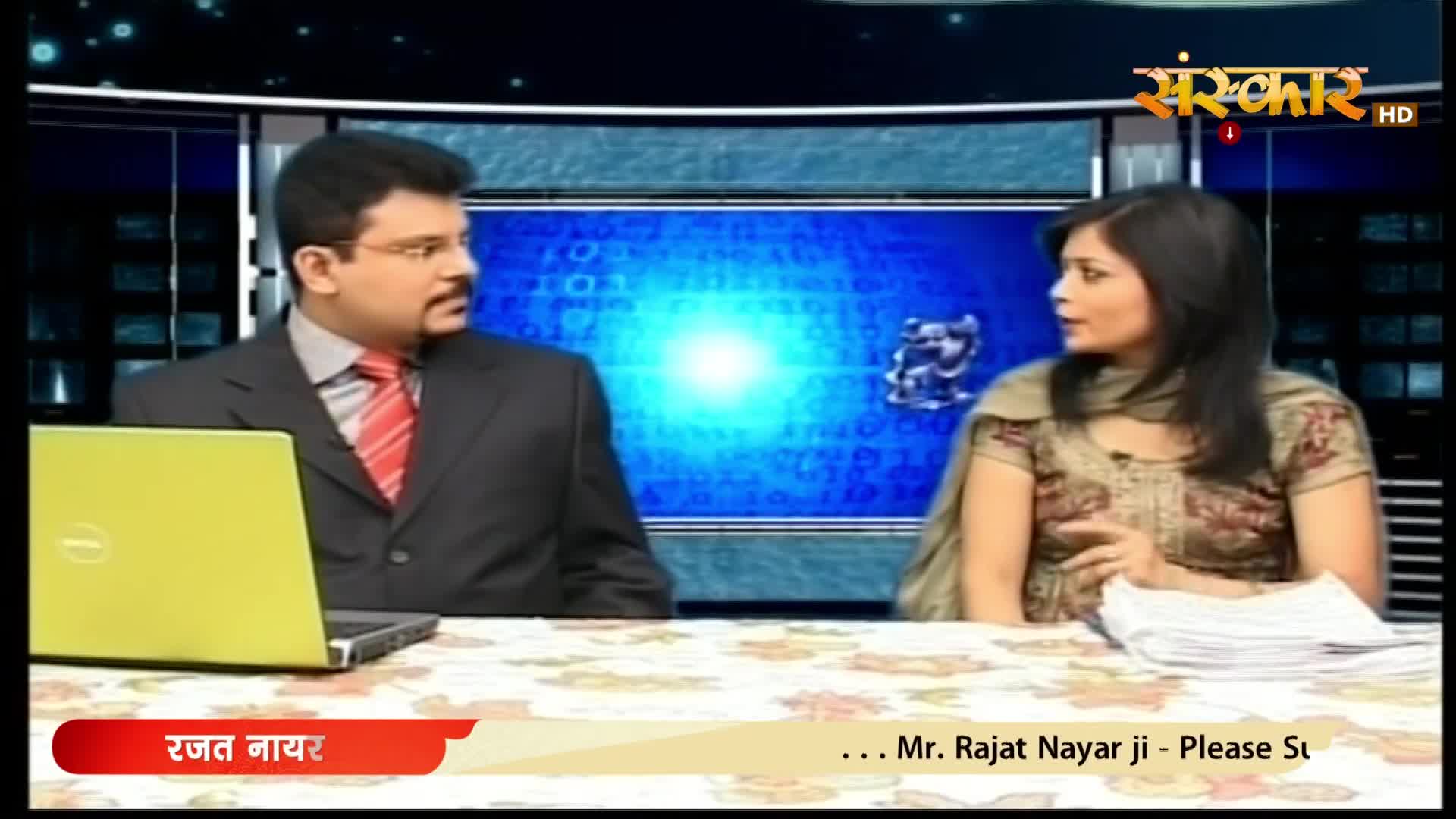 A man in a suit and tie faces a woman in a patterned salwar kameez, both seated at a table with a laptop and papers. The Sanskar HD logo is visible in the upper right corner.