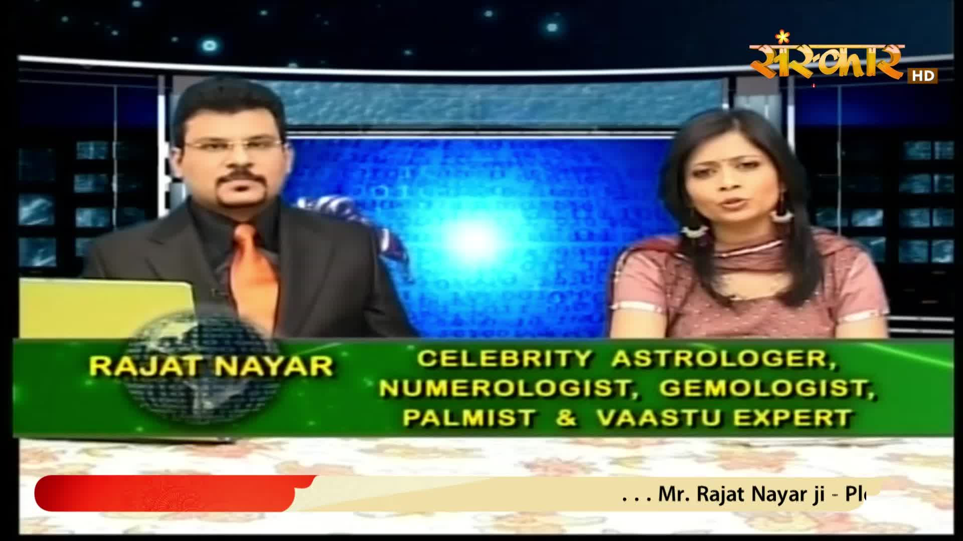 A man with a mustache and glasses, wearing a suit and orange tie, sits beside a woman in a pink outfit. A green banner below them lists "Rajat Nayar" and his credentials as a celebrity astrologer and expert.