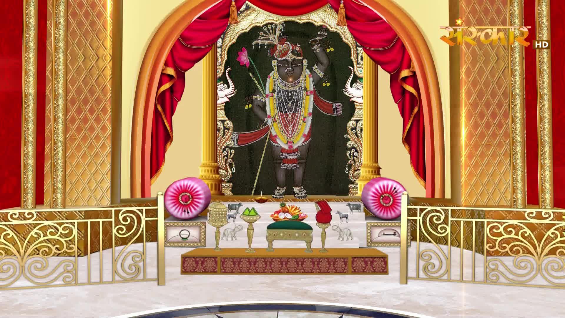 A deity stands adorned in a shrine, framed by crimson drapes and golden pillars. Offerings of fruit and a lamp sit before the altar, while decorative elephants flank the scene.