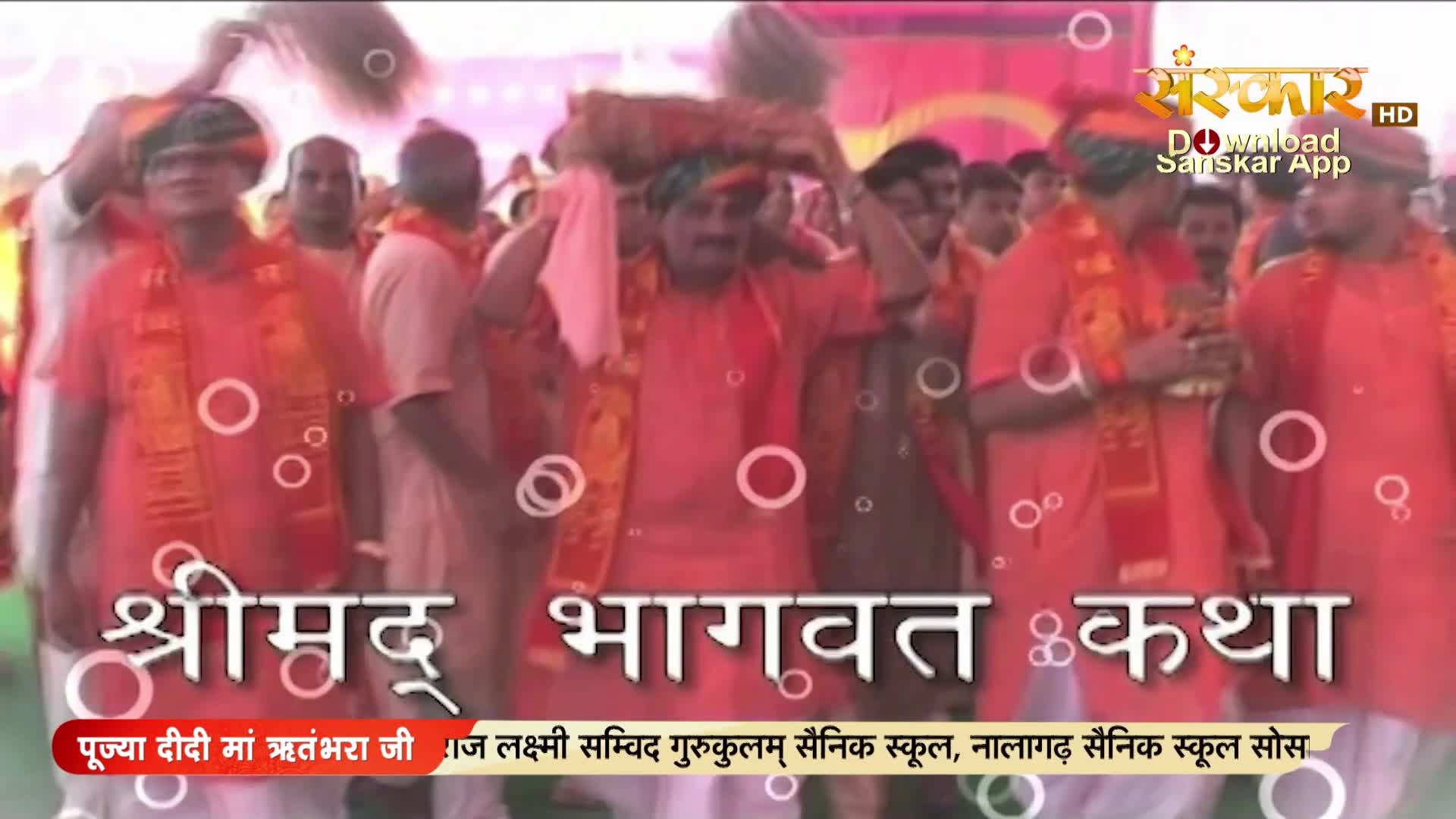 A procession moves forward, men in bright orange robes and saffron stoles carrying a bundle on their heads. The Sanskar TV logo is visible in the upper right corner.