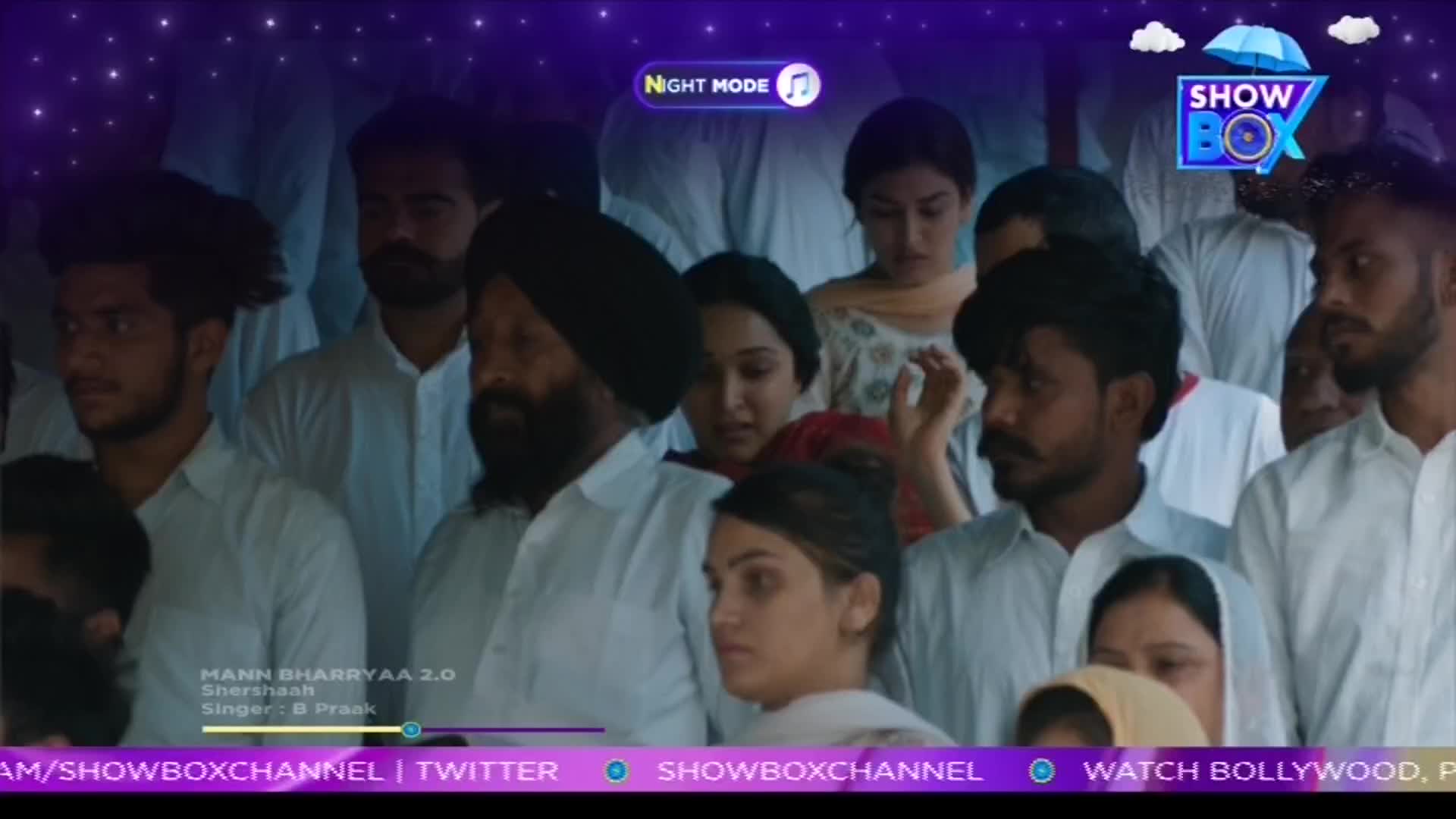 A crowd of people, many in white shirts and head coverings, are gathered together. The ShowBox logo is in the corner, and the song "Mann Bharryaa 2.0" is playing.
