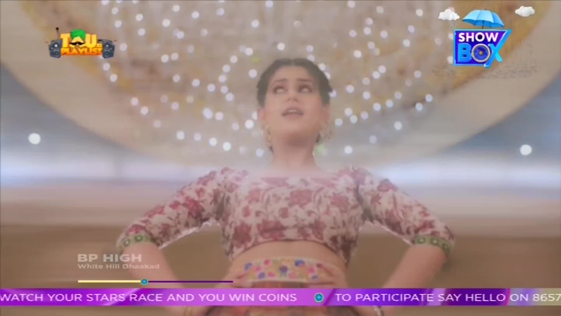 A woman in a floral top and cropped skirt stands with her arms out, looking up. The scene is part of a ShowBox broadcast, with logos and text overlaid on the image.
