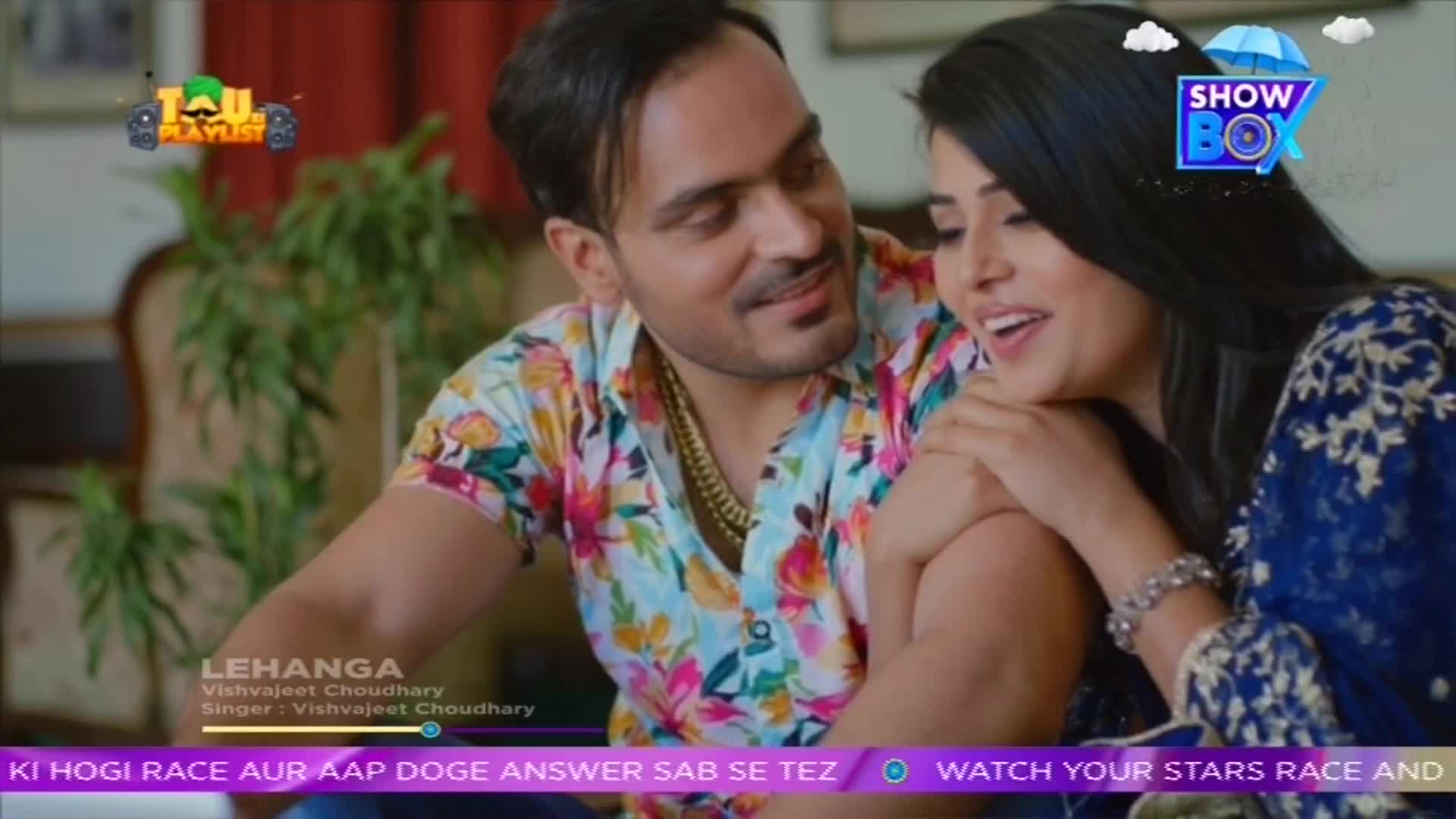 The man in the floral shirt leans in, smiling at the woman beside him. They are both looking to the side, as if watching something on the screen of the Indian music channel, ShowBox.
