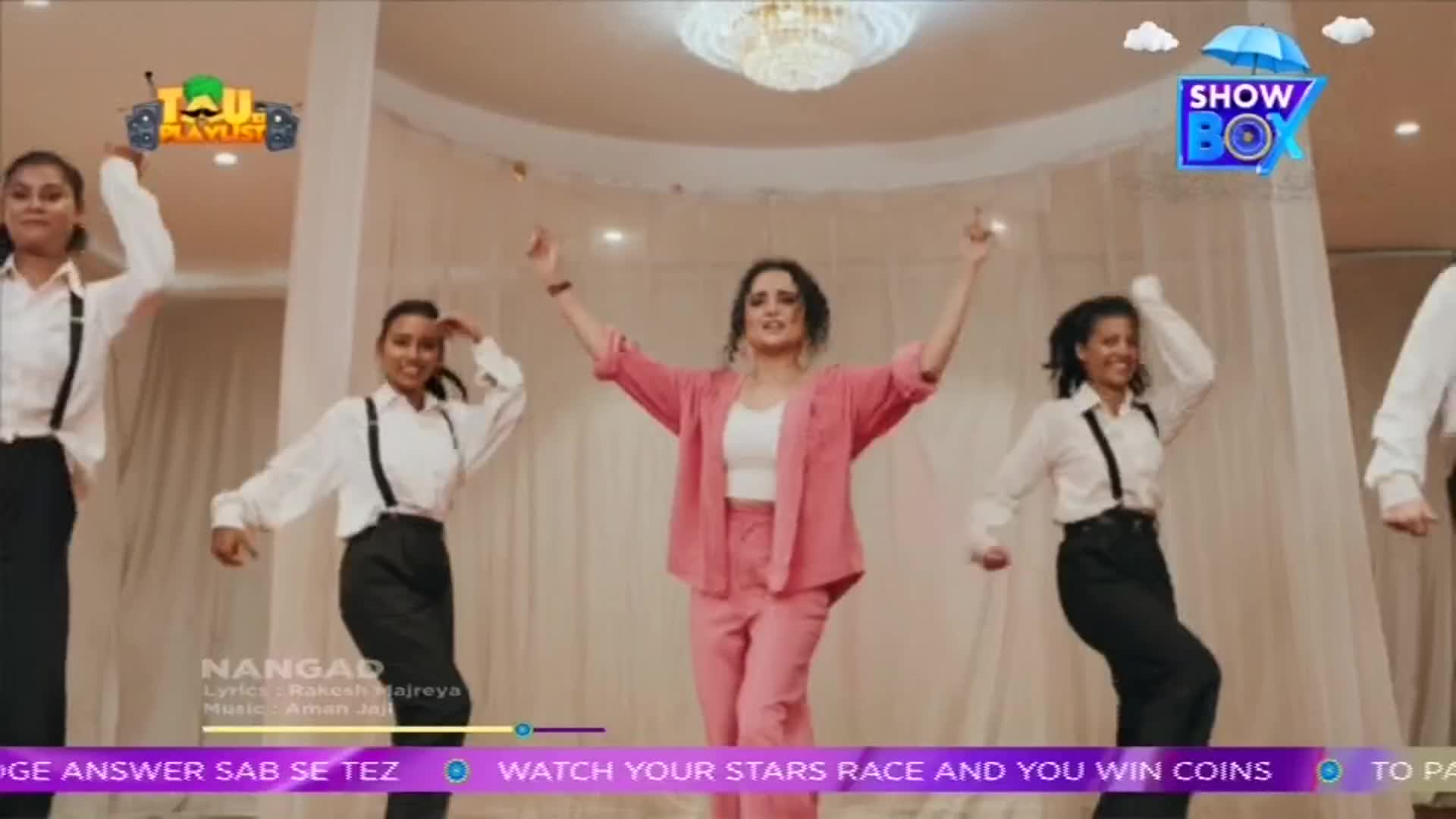 A woman in a pink suit stands center, arms raised, as she leads a group of dancers in white shirts and black pants. The ShowBox logo floats in the corner as a song plays.
