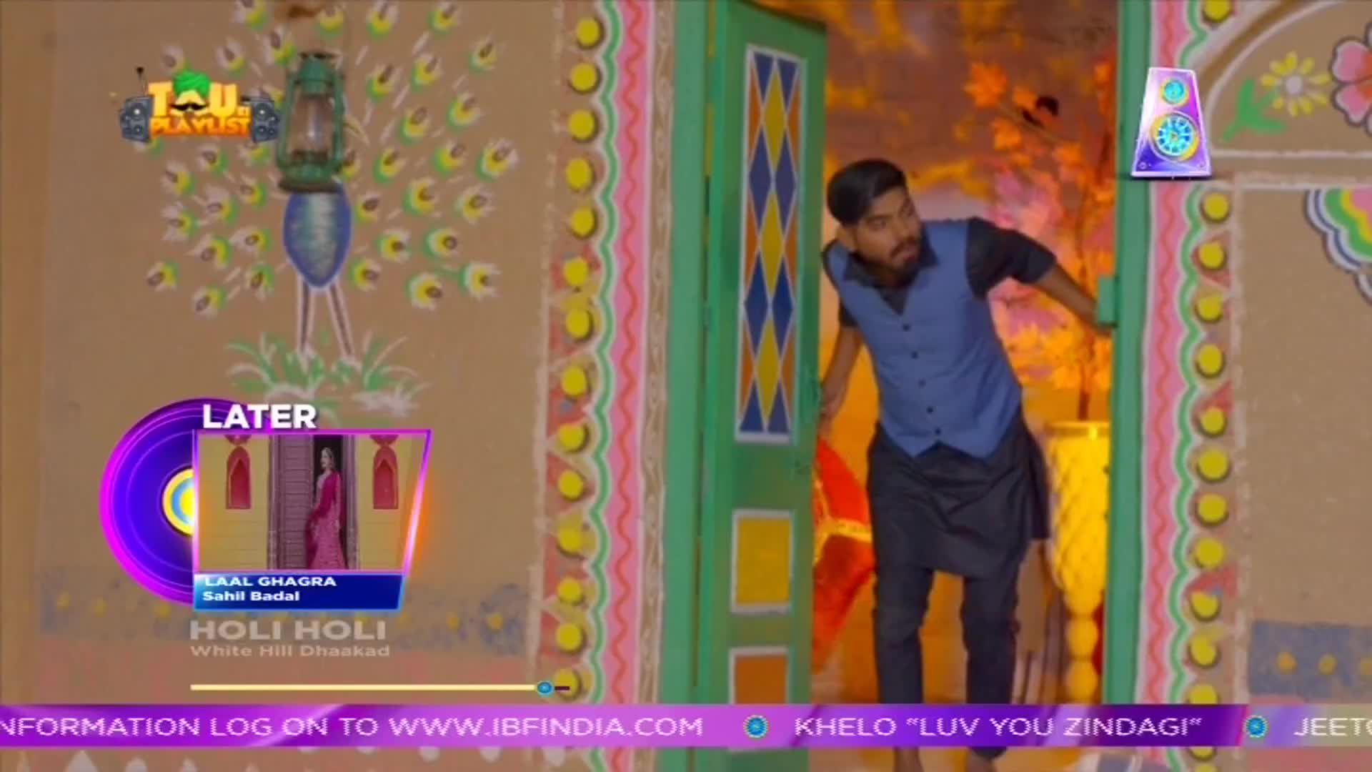 A man in a blue vest and black pants peeks out from behind a brightly painted door, as if surprised. A ShowBox logo and a preview of a music video for "Laal Ghagra" are visible on the screen.
