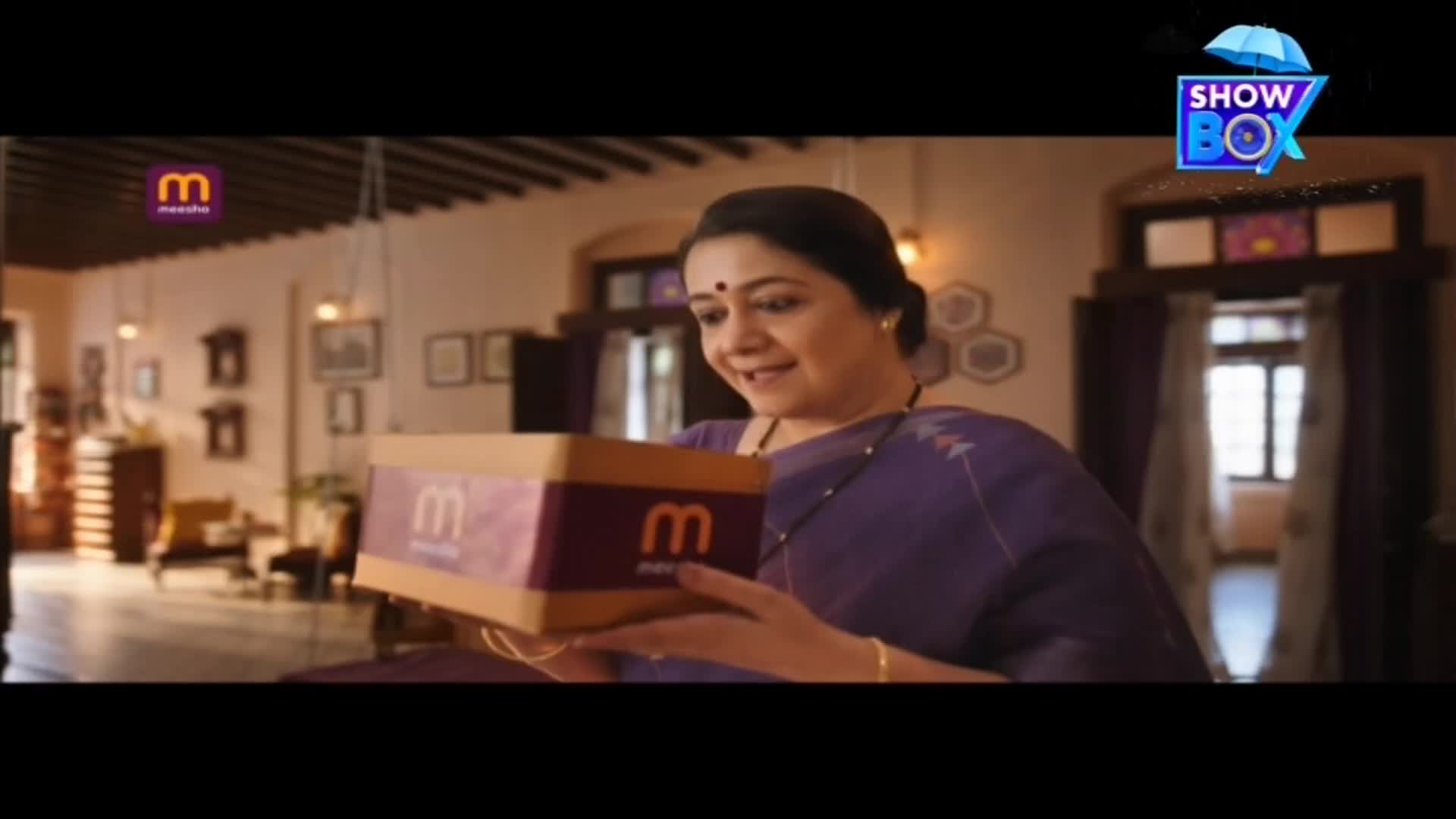 A woman in a purple sari holds a box with a logo, smiling at it. The scene appears to be an advertisement, possibly from India, airing on ShowBox.

