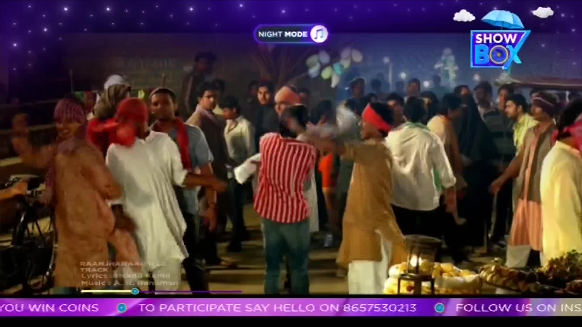 A crowd of people in India are dancing to a song on ShowBox, their arms and bodies moving to the music. The scene is lit with a warm glow, and the energy is high.
