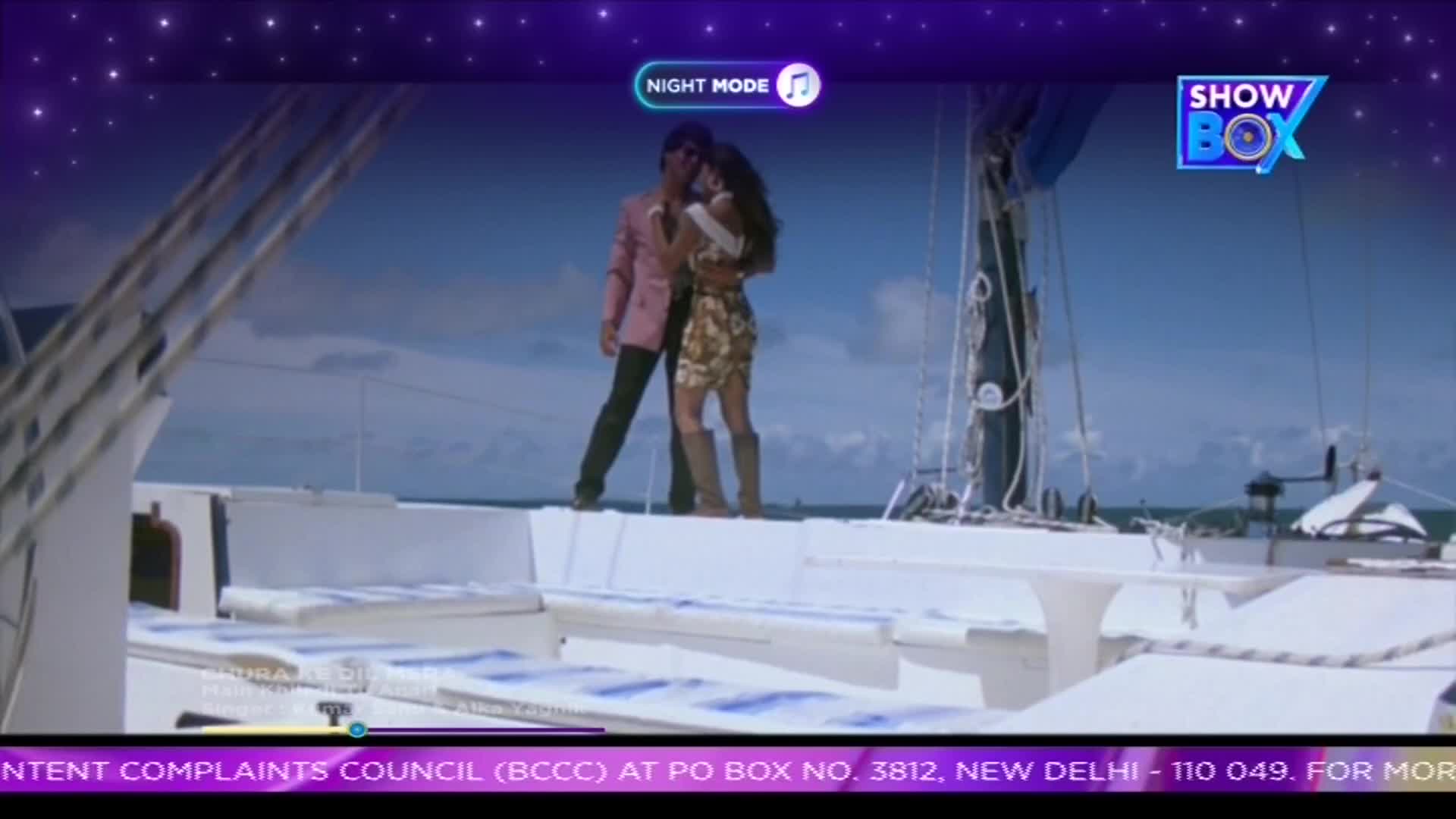 On a boat, a man in a pink jacket and a woman in a patterned dress embrace, with the sea and sky as their backdrop. The "ShowBox" logo sits in the corner, and the screen suggests a film from India.
