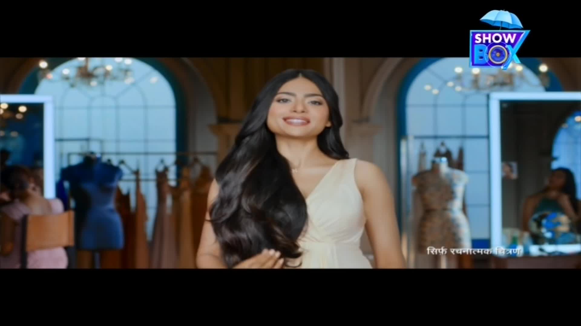 A woman in a cream dress smiles, her long, dark hair cascading over her shoulders. The ShowBox logo floats in the upper right corner, and the scene seems to be set in a fashion studio in India.
