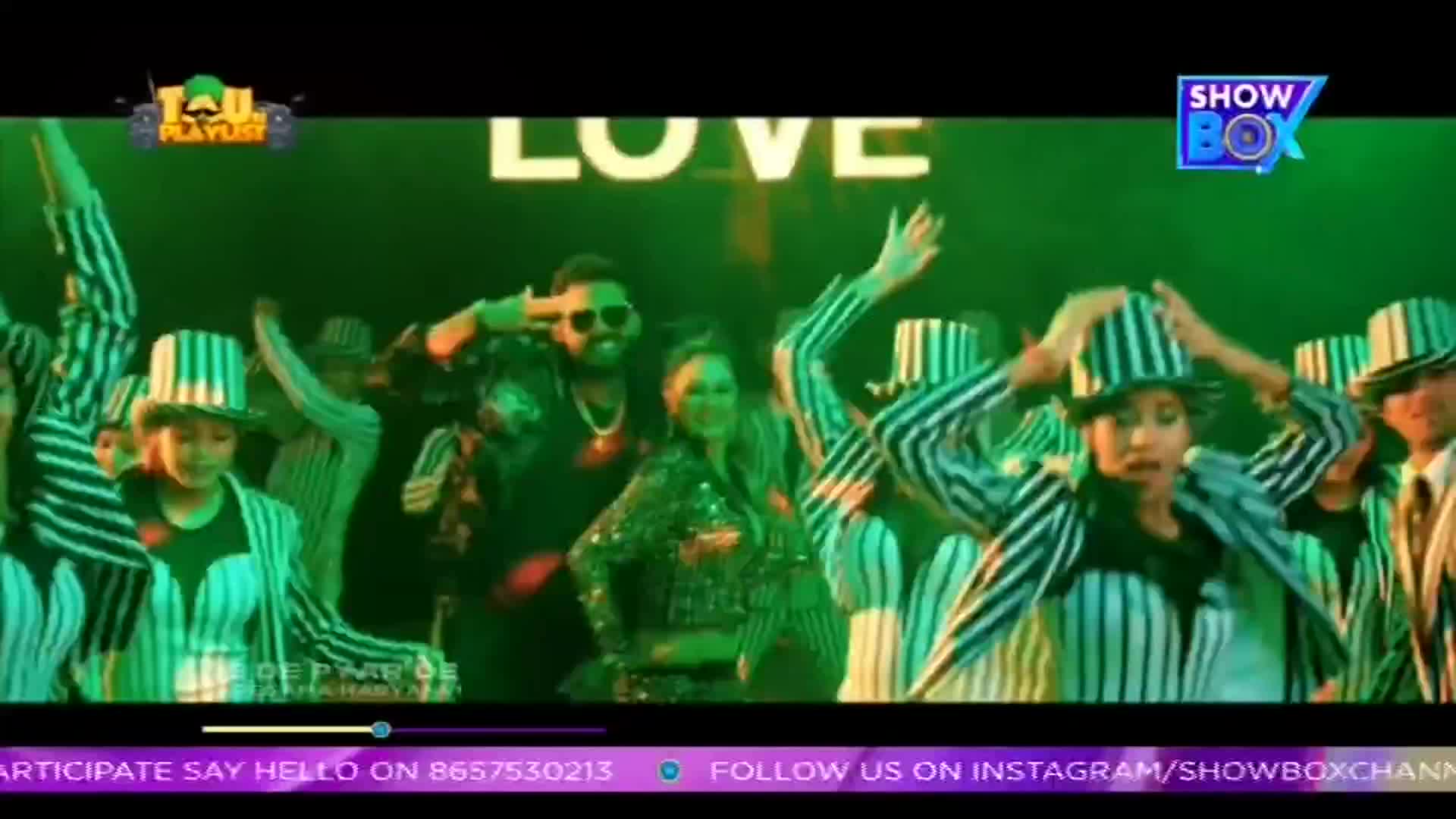 A group of dancers in striped suits and hats move in unison, their arms raised. A couple in the center, surrounded by the ensemble, seem to be the focus of this ShowBox music video.
