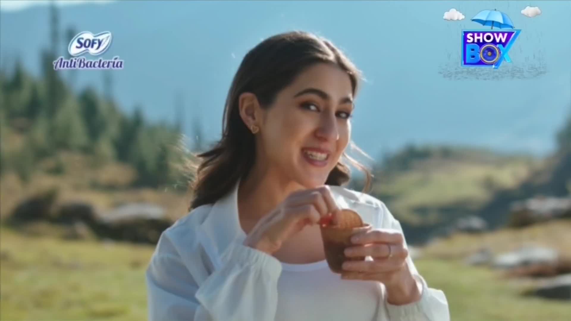 A woman smiles, holding a small cup with a snack, possibly a cookie, in her hands. The background shows a mountain range, and the ShowBox logo is visible in the corner.

