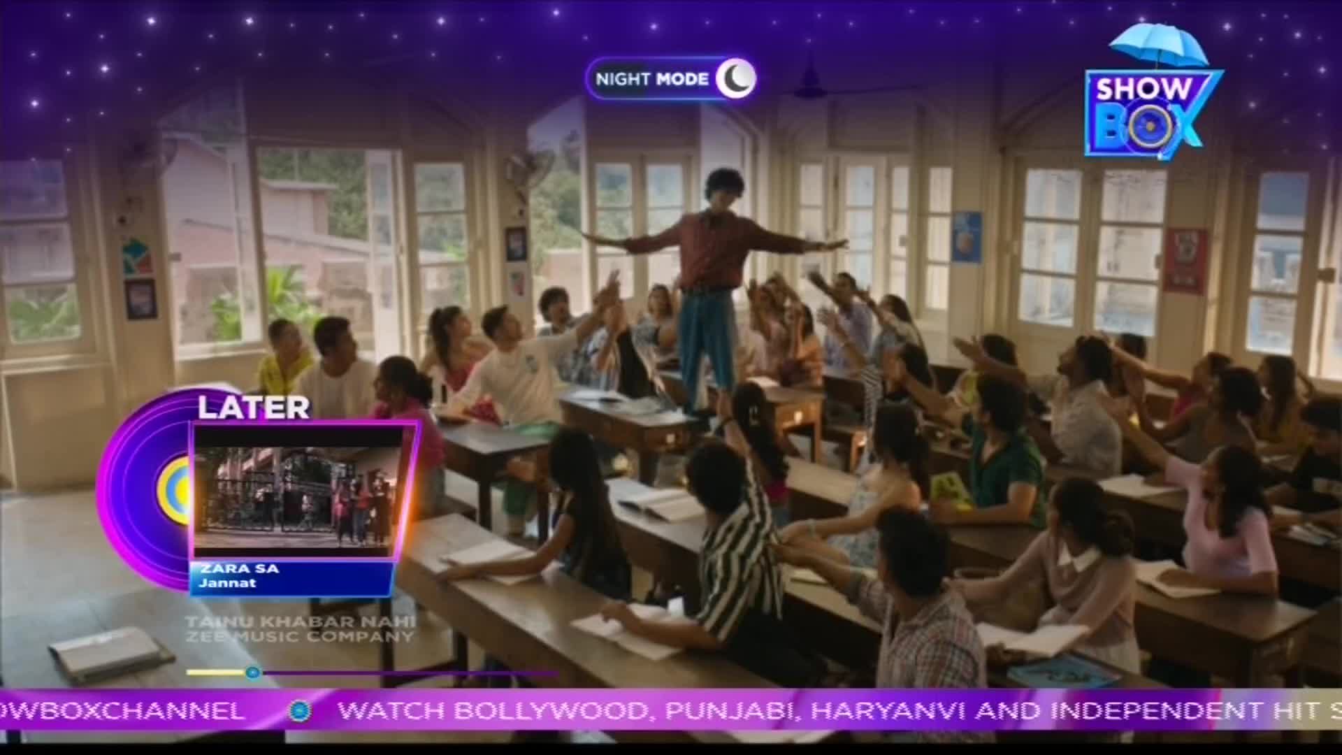 A man stands on a desk with his arms outstretched, while students in a classroom reach towards him. The ShowBox logo sits in the top right corner, and a "Later" screen displays a music video.
