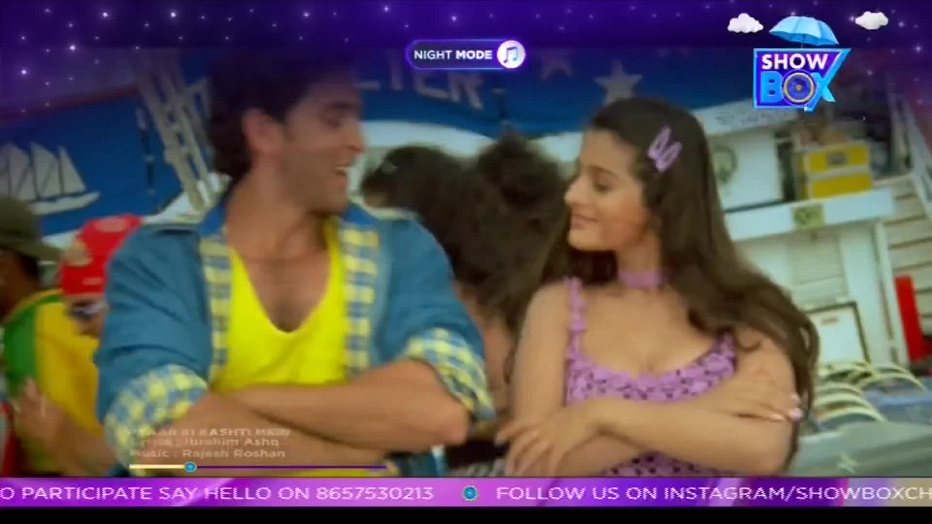 A man in a yellow shirt and a woman in a purple dress are smiling at each other, framed by a "ShowBox" logo. The scene, lit by a night mode filter, looks like a still from a Bollywood music video.
