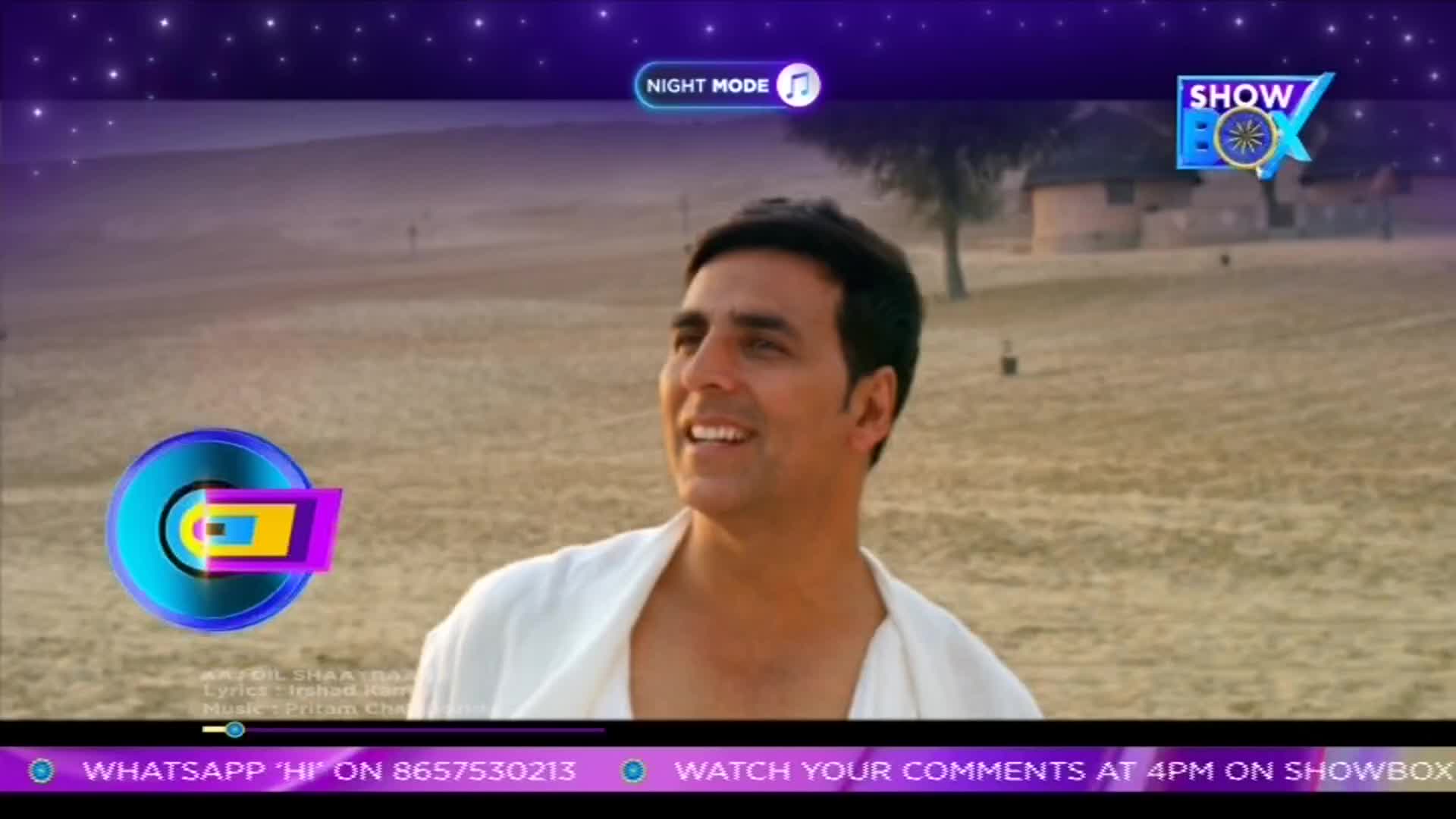 Akshay Kumar smiles, looking off-screen, while a song graphic plays on ShowBox. The scene is set in a dusty landscape, and the "Night Mode" icon suggests it's nighttime.
