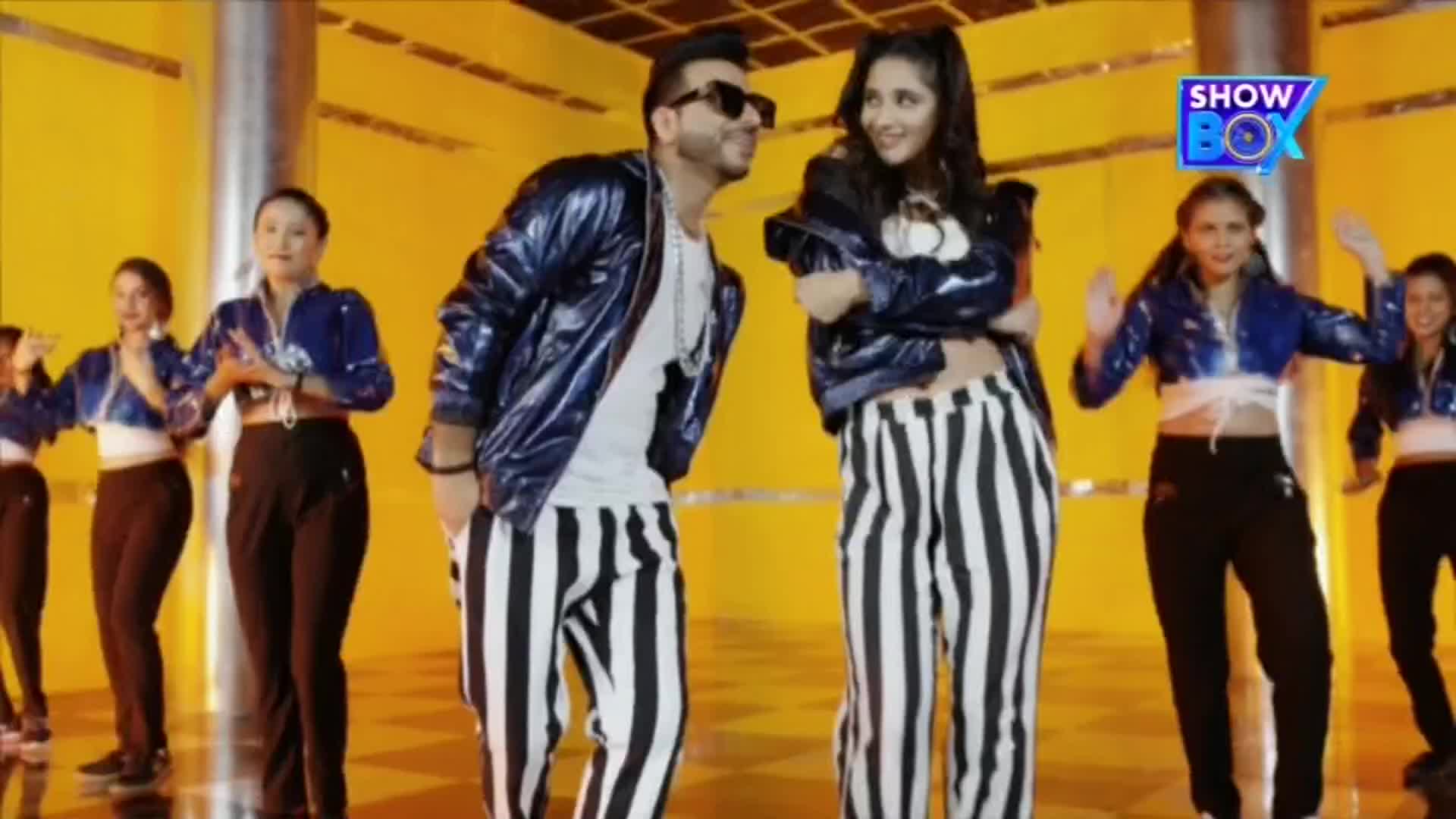 A man and woman in matching striped pants and shiny jackets dance in front of a group of backup dancers. The ShowBox logo is in the corner, and the set is brightly lit.
