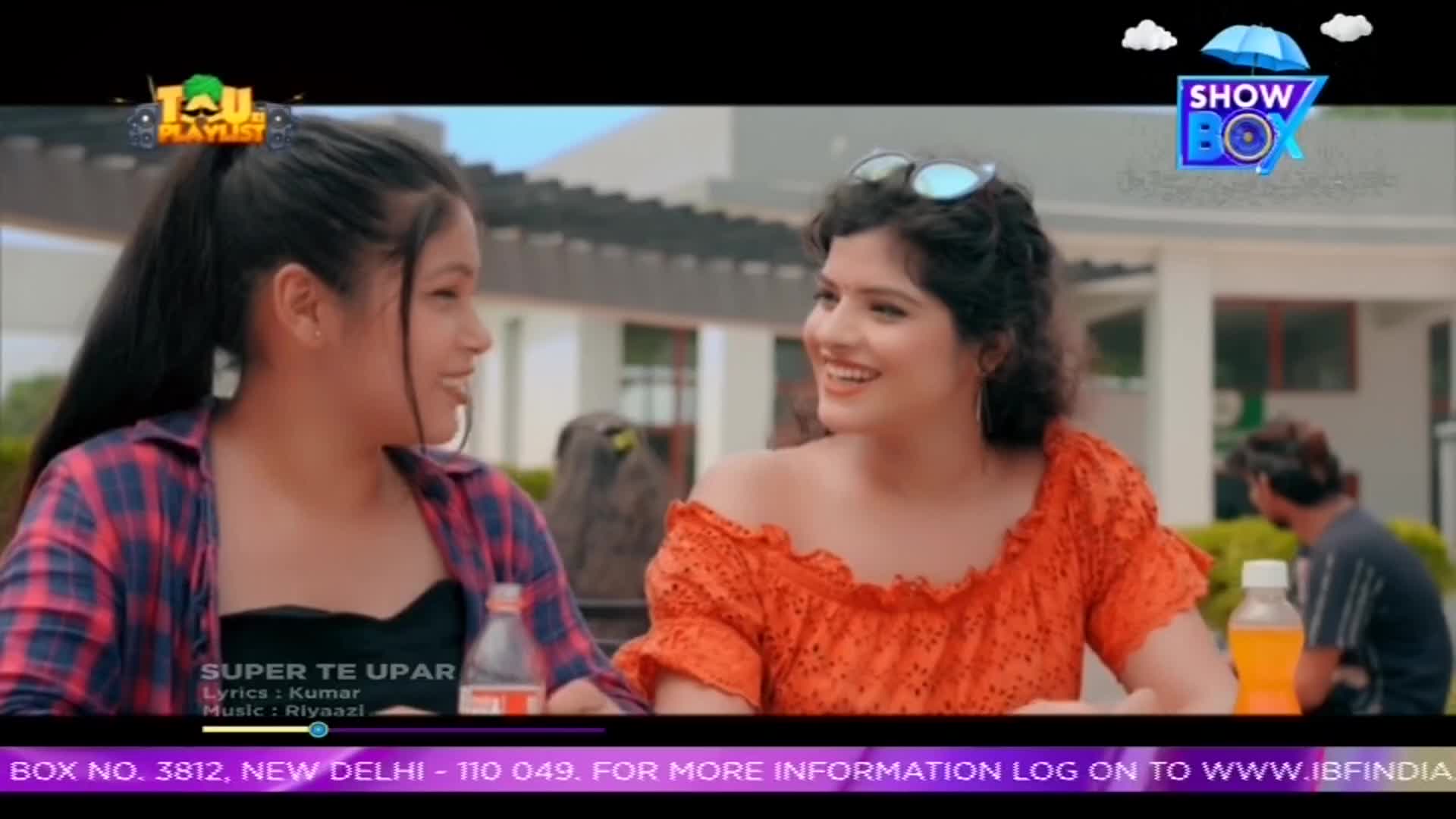 Two young women are laughing and chatting, sitting outside near a table with drinks. The ShowBox logo is visible in the corner, and a song title, "Super Te Upar," is displayed at the bottom of the screen.
