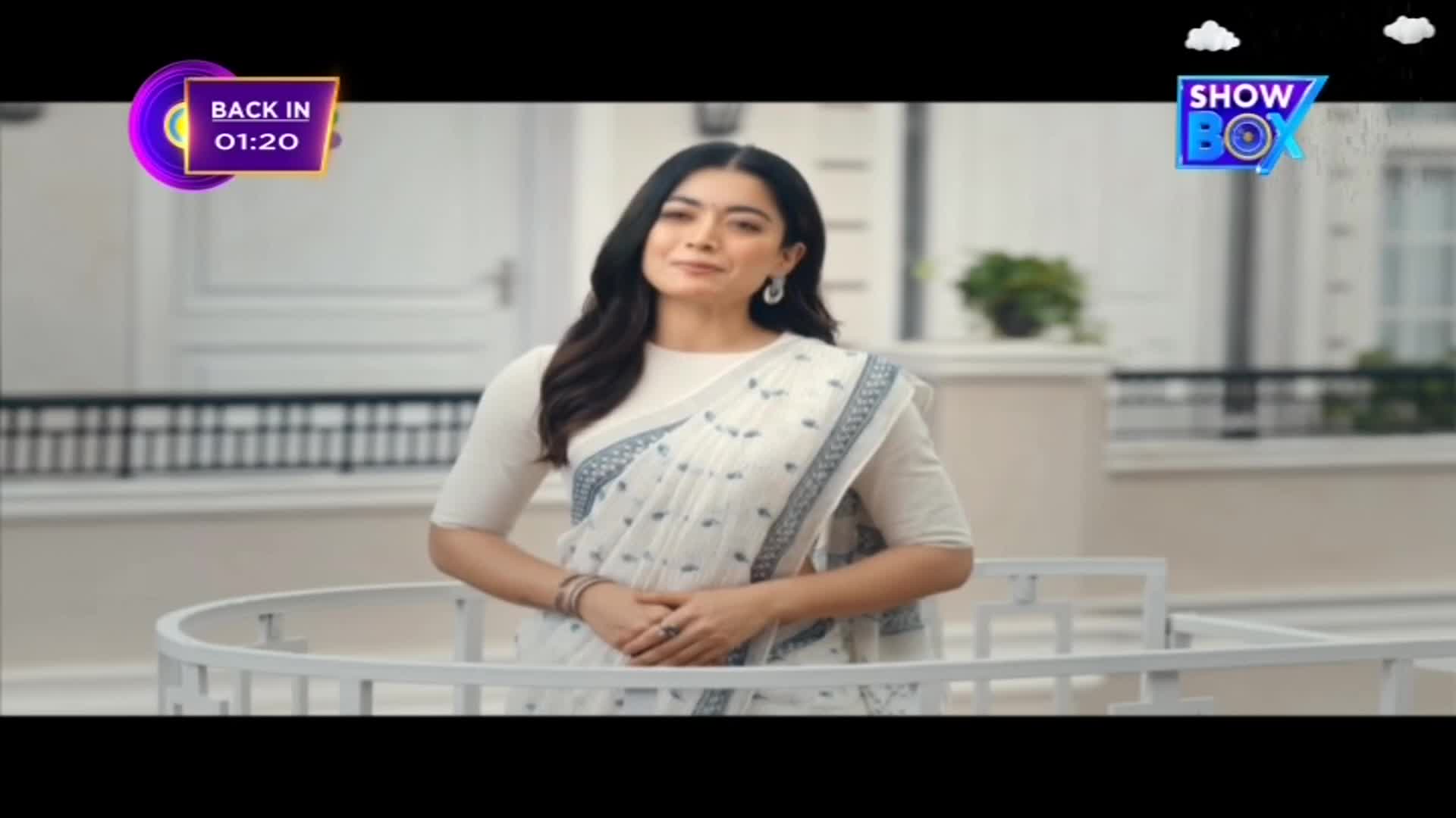 A woman in a white saree stands on a balcony, smiling at the camera. The ShowBox logo is visible, and a timer in the corner counts down.
