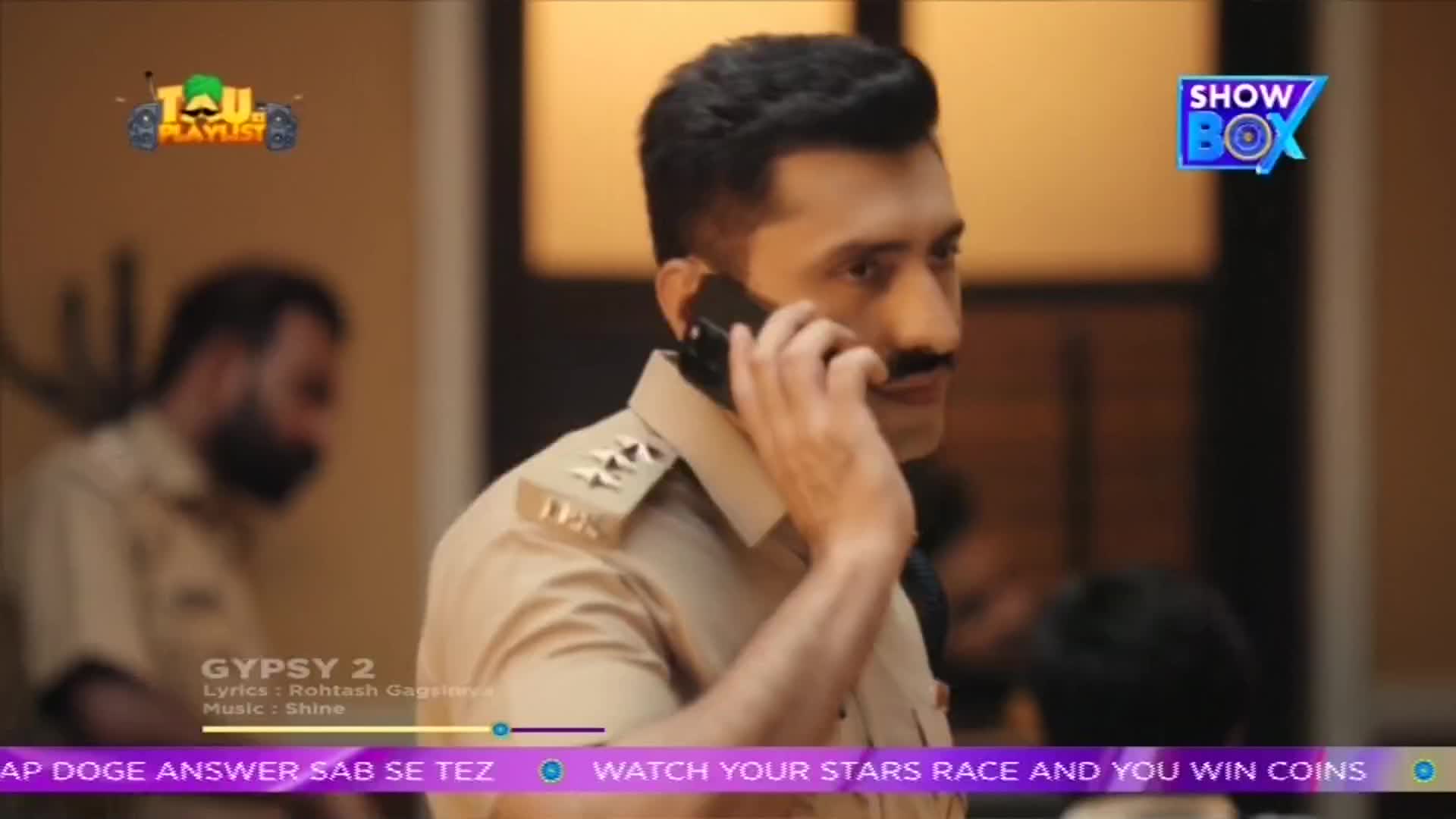 A man in a police uniform holds a phone to his ear, his mustache prominent. The ShowBox logo is visible in the upper right corner, and a music playlist graphic is in the upper left.
