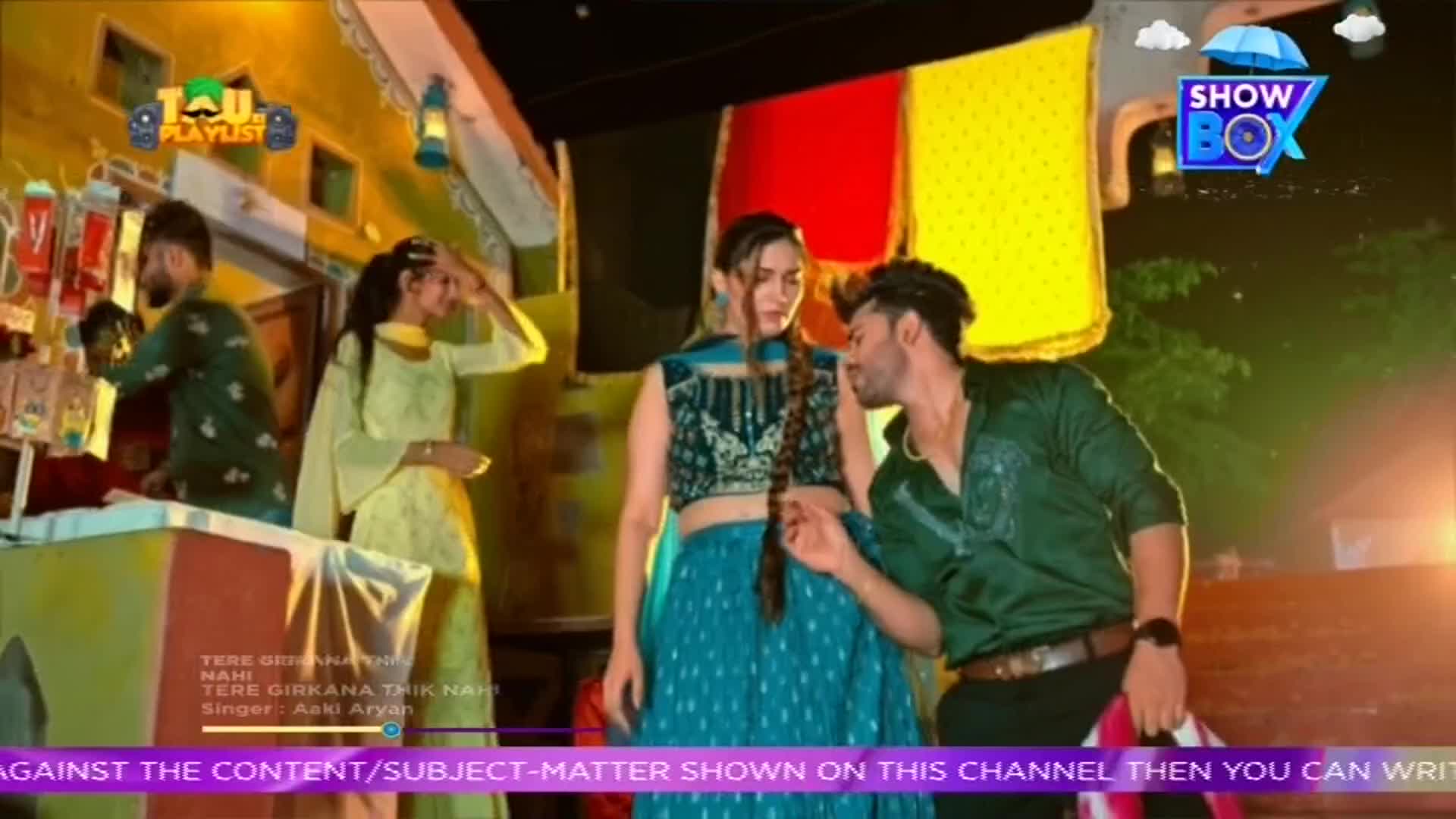 A man in a green shirt leans in close to a woman in a teal outfit, as if whispering. The scene looks like it's from a music video, with a "ShowBox" logo in the corner and a "TAU PLAYLIST" logo on the top left.
