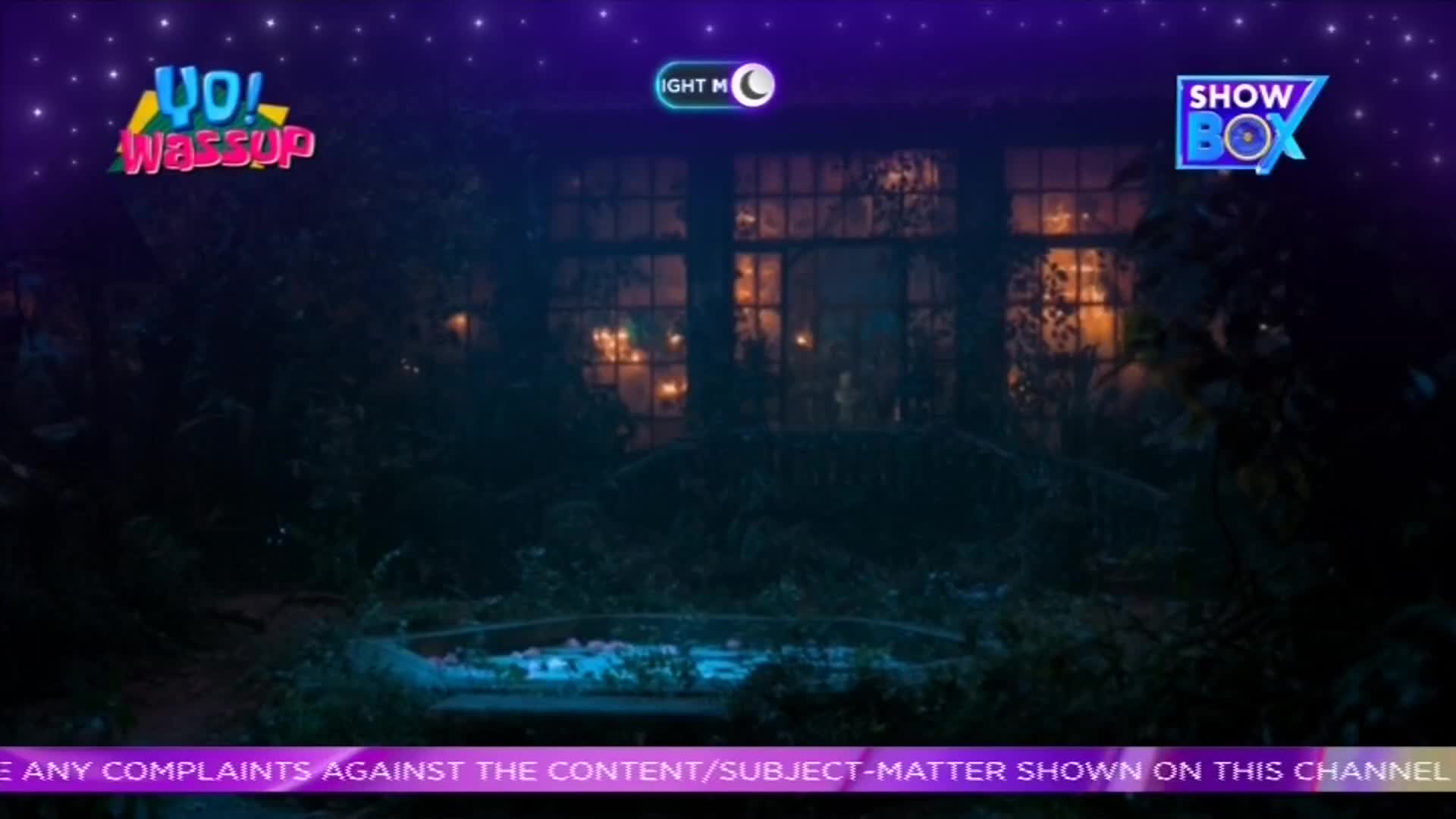 ShowBox's logo sits in the corner, with "Yo! Wassup" above a dark, overgrown garden. Warm light spills from the windows of a house, and a small pool reflects the glow.
