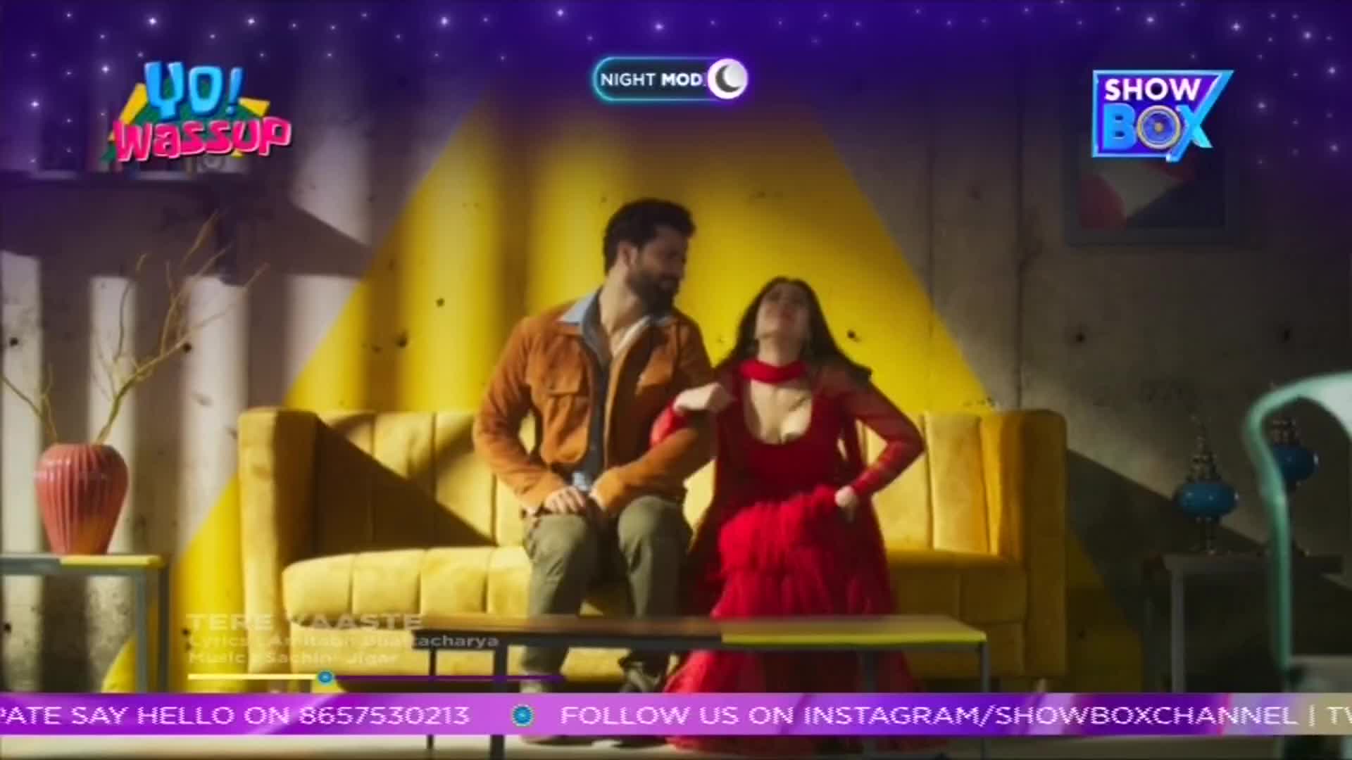 A man in a brown jacket sits beside a woman in a red dress on a yellow couch. They are posed, seemingly for a ShowBox segment, against a backdrop with a "Night Mode" graphic.
