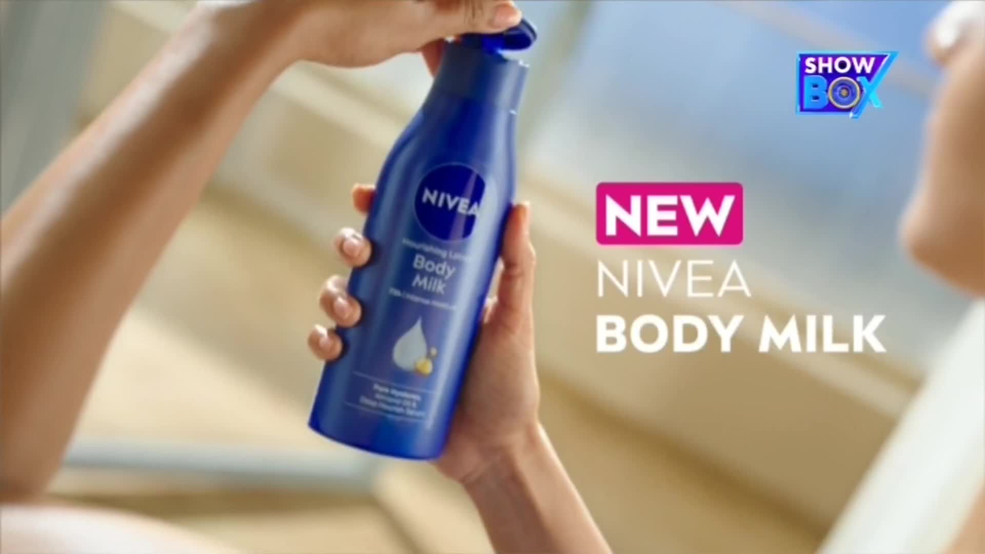 A hand is opening the blue cap of a Nivea Body Milk bottle. The "ShowBox" logo is visible, and the words "NEW NIVEA BODY MILK" are displayed on the right.
