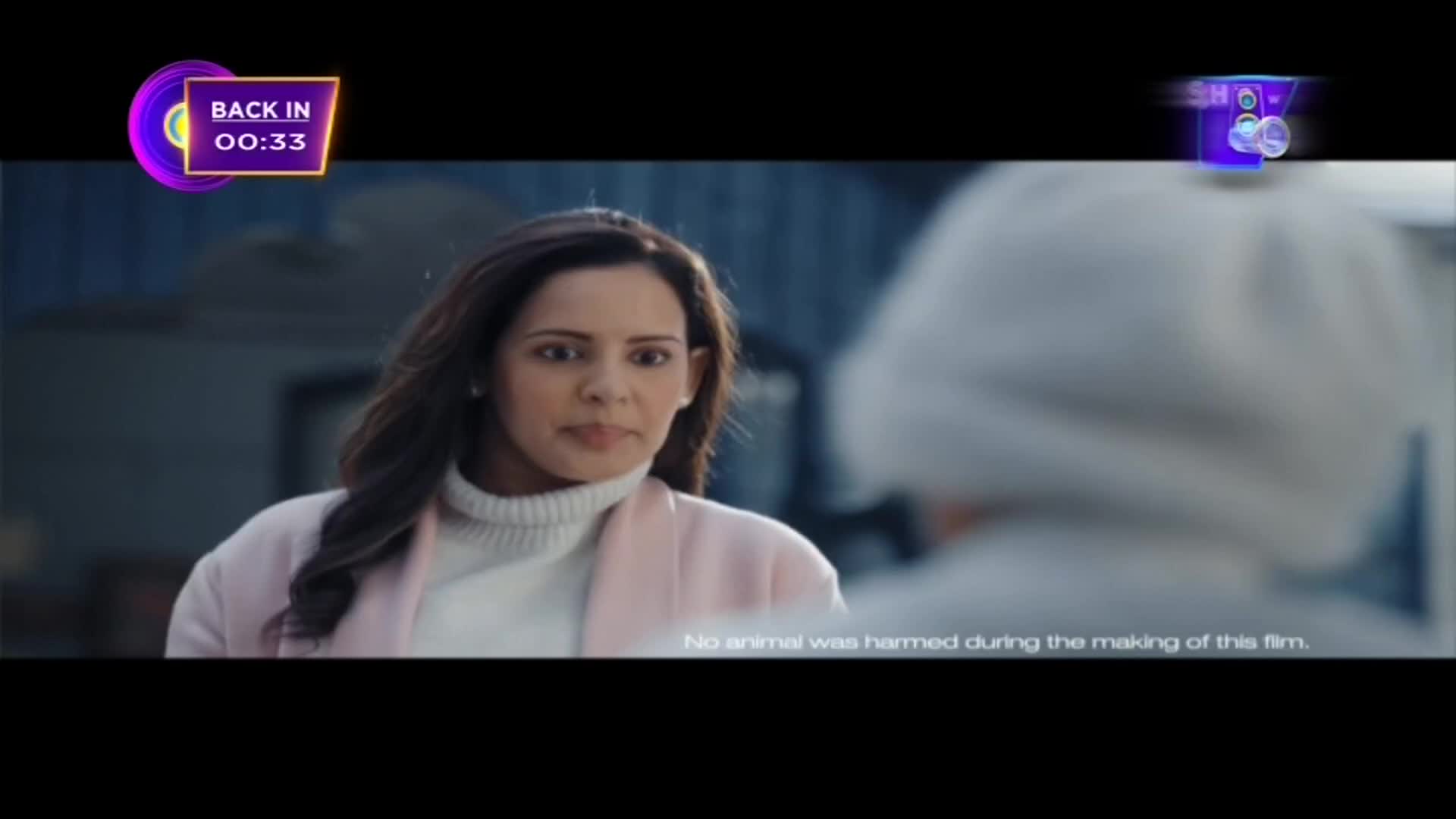 A woman in a pink coat and white turtleneck stares intently at someone out of frame. The ShowBox logo is in the corner, and a countdown timer indicates a return from a break.
