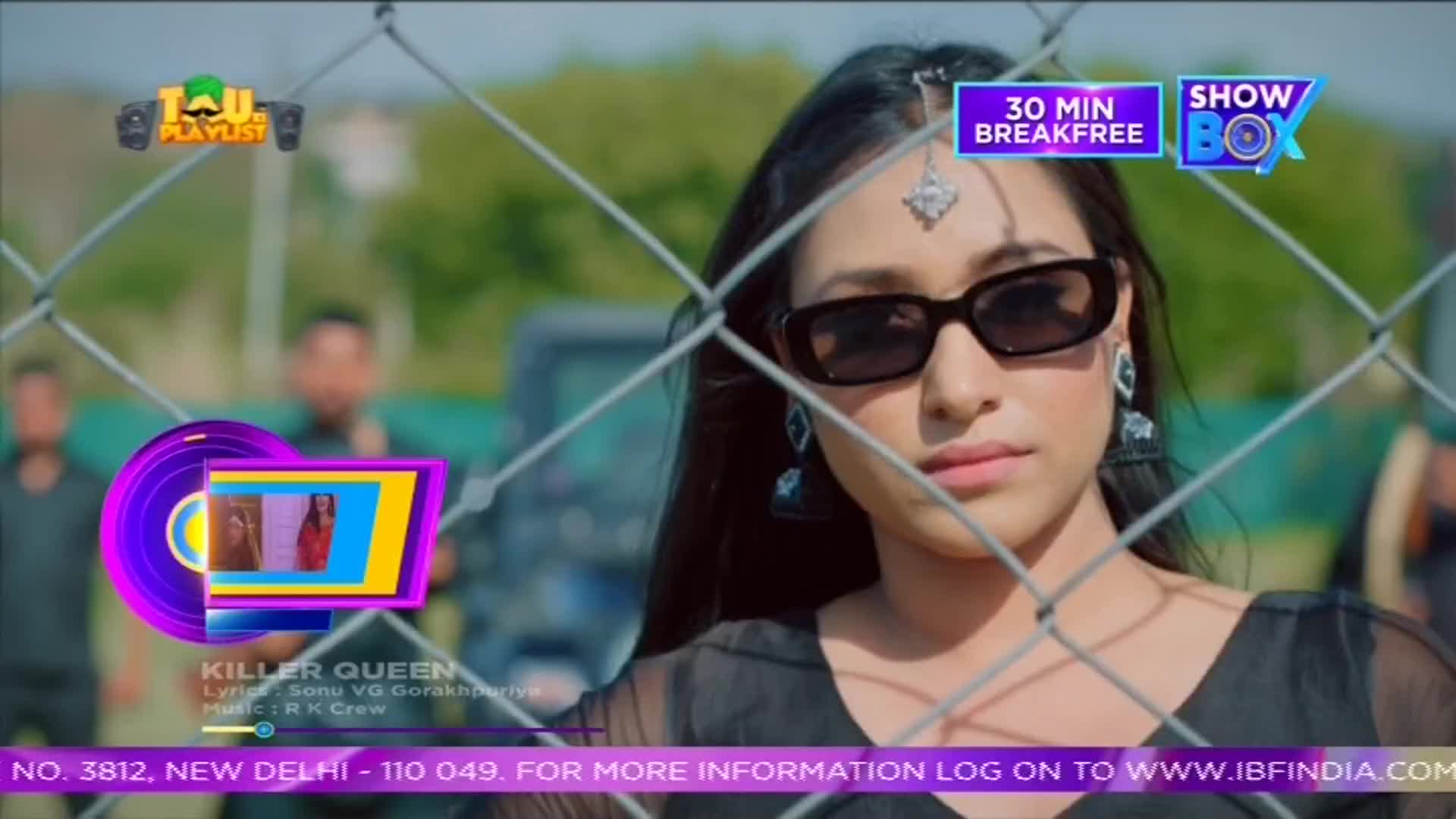 A woman in sunglasses stares directly at the camera, framed by a chain-link fence. The scene is from a music video, with the ShowBox logo and "Killer Queen" text overlaid on the image.
