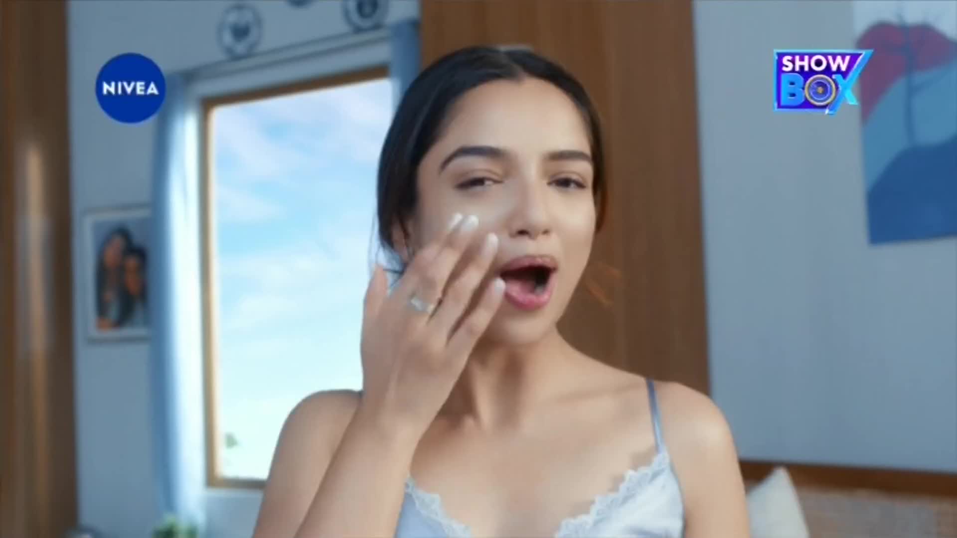 A woman in a light blue tank top is applying cream to her face, her mouth slightly open. The Nivea logo and the ShowBox logo are visible in the frame.
