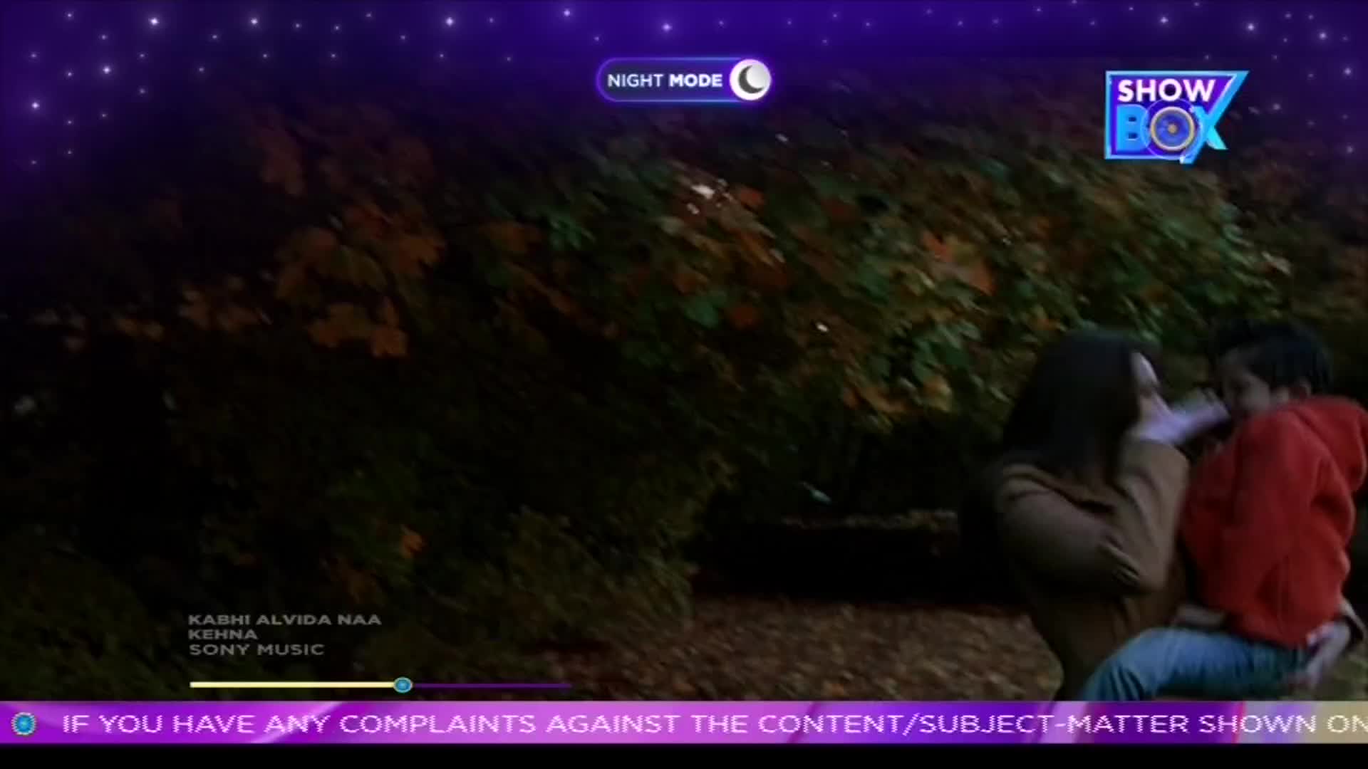 A woman in a brown coat holds a child in a red hoodie, their faces close. The scene is playing on ShowBox, with a night mode setting and music credits scrolling at the bottom.
