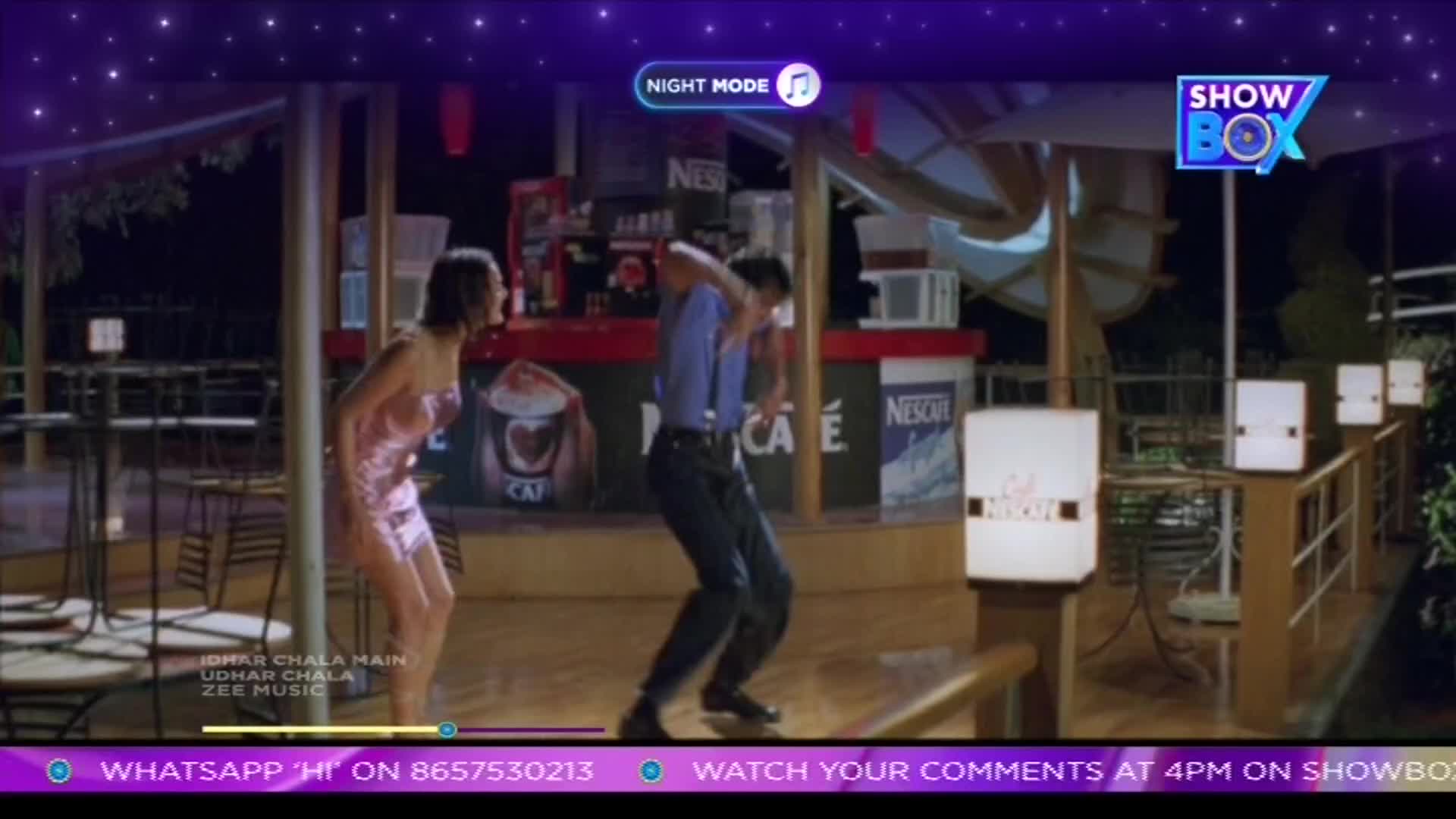 A man in a blue shirt and dark pants dances with a woman in a pink dress. They are outside a cafe at night, with a ShowBox logo visible.