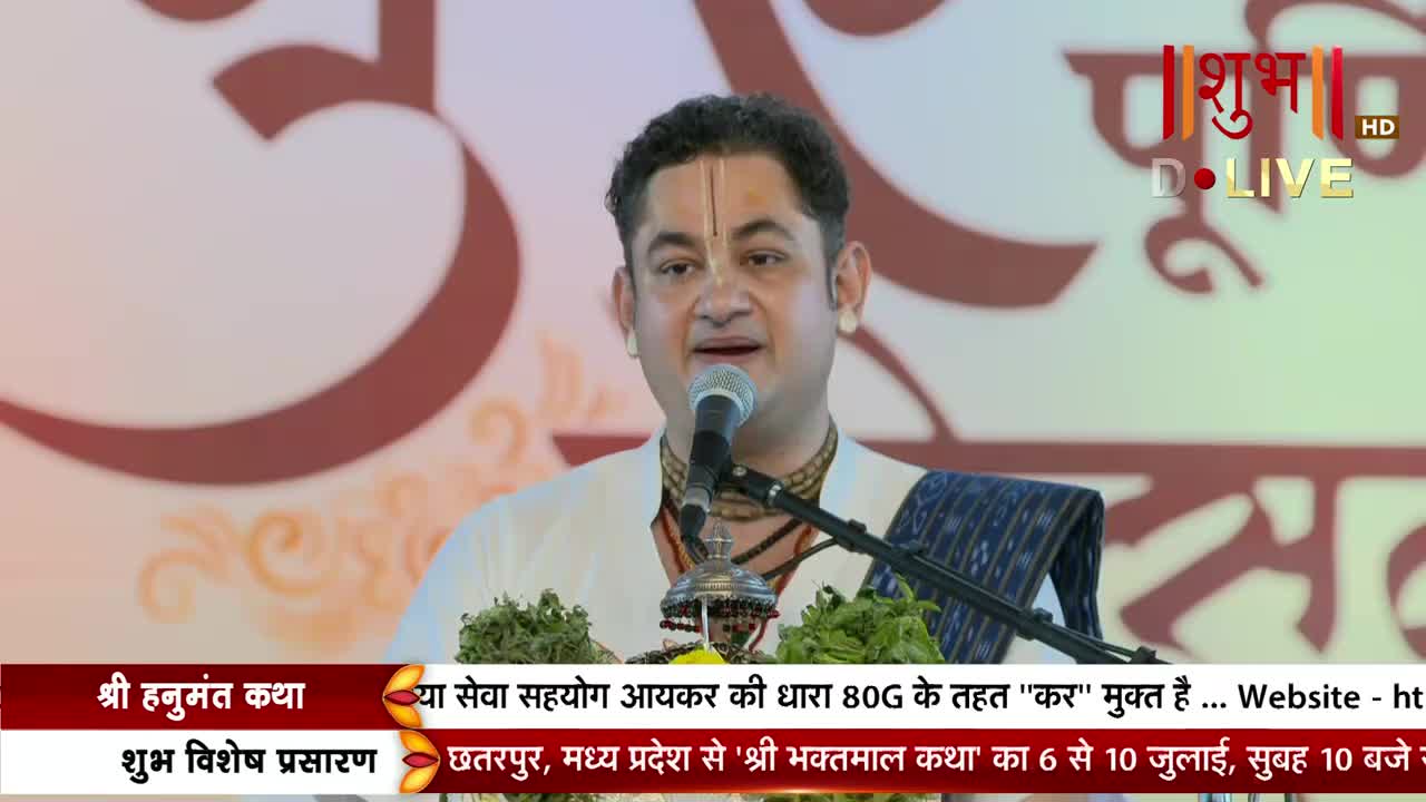 The man is speaking into a microphone, his expression animated. Below, the Shubh TV logo and text about an event in India are visible on the screen.
