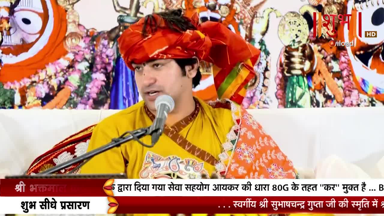 A man in a vibrant turban and yellow shirt speaks into a microphone, his words broadcast live on Shubh TV. The broadcast appears to be from India and is dedicated to the memory of a man named Subhashchandra Gupta.
