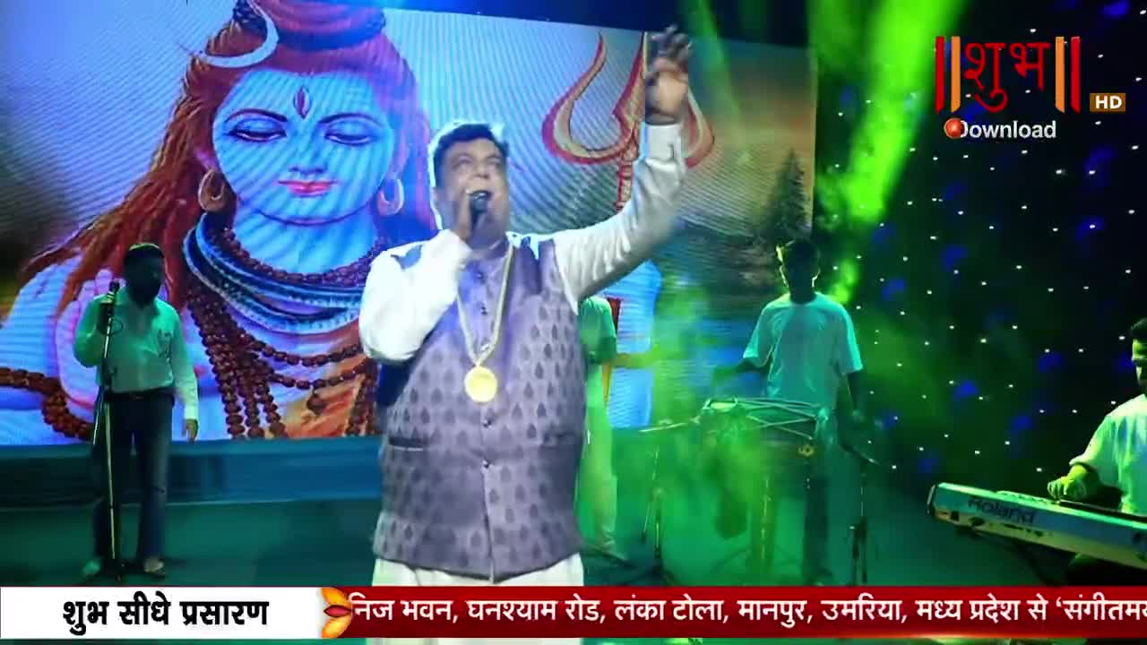 The man in the patterned vest sings into a microphone, his right arm raised. Behind him, a large screen displays an image of a deity, and the Shubh TV logo is visible in the corner.
