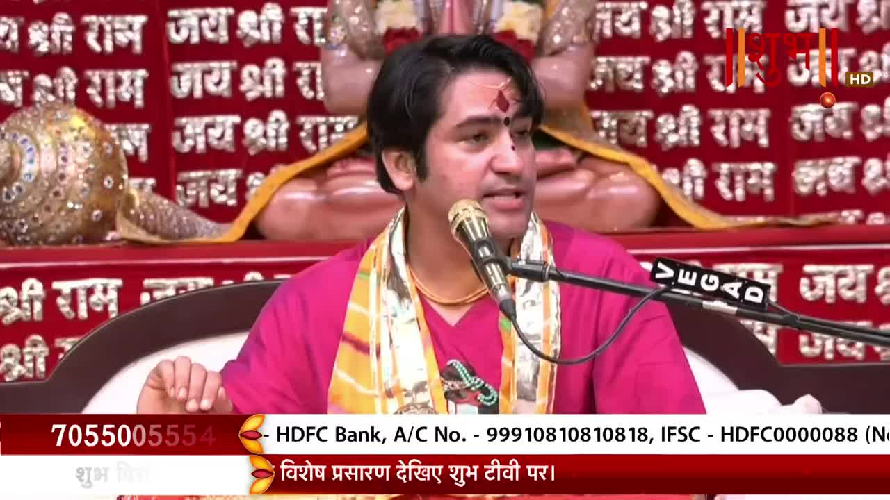A man in a pink shirt and a scarf speaks into a microphone, his words broadcast on Shubh TV in India. Behind him, a red backdrop displays religious text.
