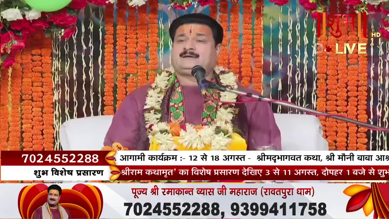 A man in a maroon shirt speaks into a microphone, a garland of flowers around his neck. The Shubh TV logo is visible, and text below the speaker advertises an upcoming event.
