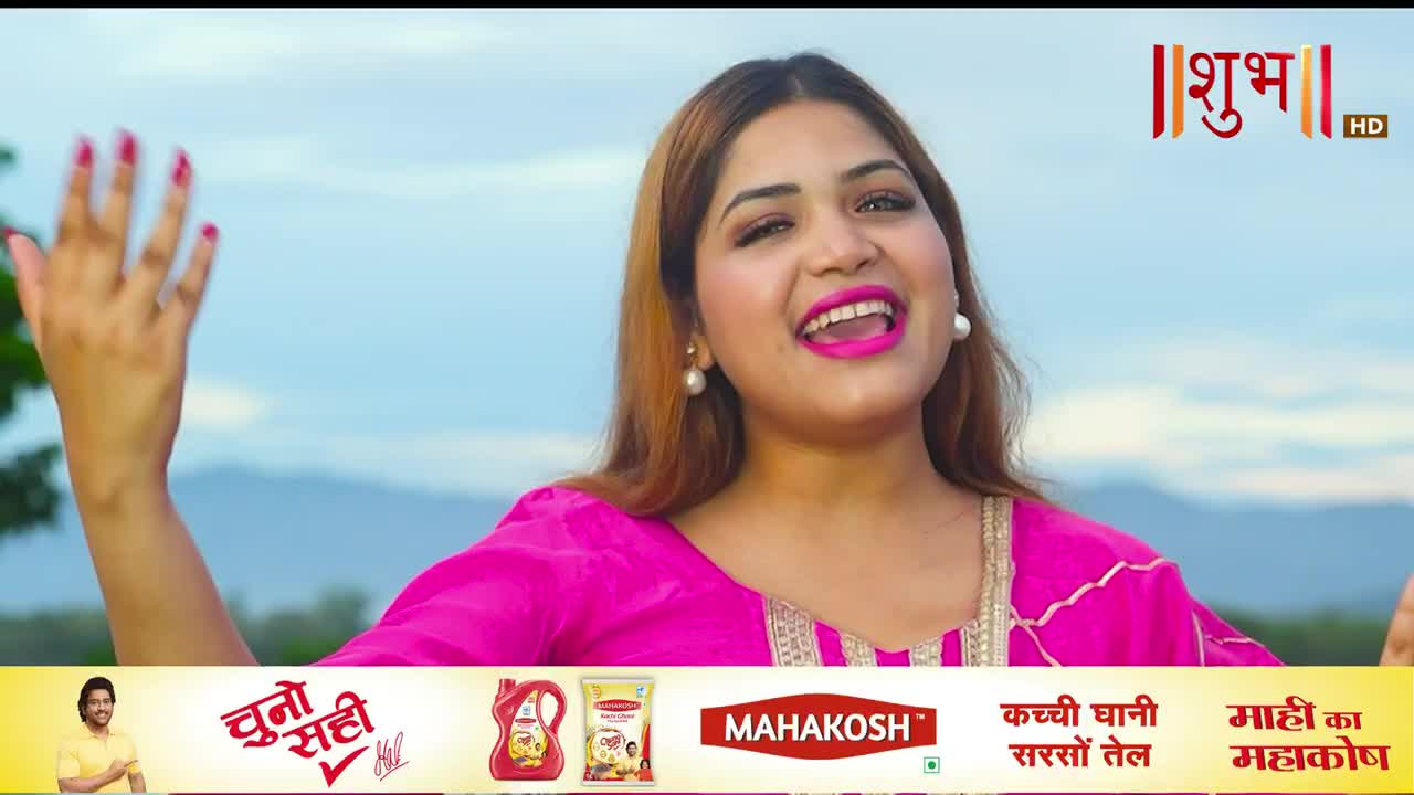 The woman in the bright pink outfit sings with her mouth wide open, her hand raised in a wave. Behind her, the sky is a soft blue, and the Shubh TV logo sits in the corner.
