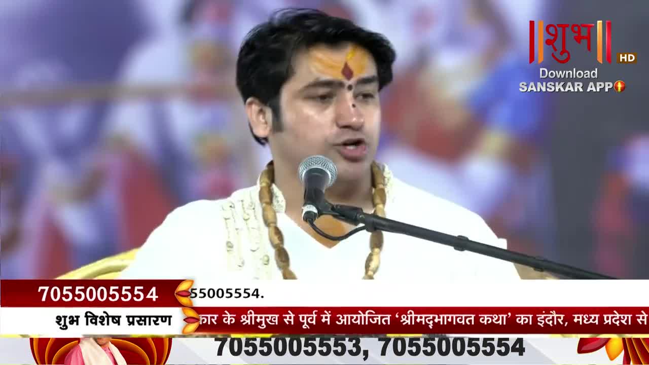 A man wearing a tilak speaks into a microphone, his mouth moving as he addresses the audience. The broadcast is on Shubh TV, with contact information and event details displayed at the bottom of the screen.
