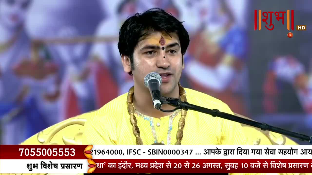 A man in a yellow shirt speaks into a microphone, a small red dot on his forehead. The Shubh TV logo is visible in the corner, and text scrolls along the bottom of the screen.
