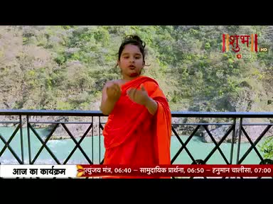 A young person in an orange robe gestures towards the camera, standing on a metal railing overlooking a river. The Shubh TV logo is visible, along with program details in Hindi.
