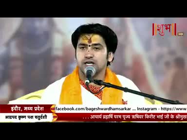 A man in a white shirt and orange scarf speaks into a microphone, his forehead marked with a dot. The Shubh TV logo is visible in the upper right corner.
