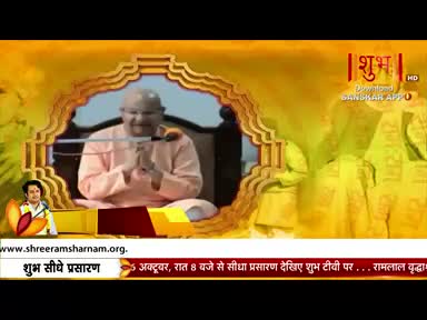 A man in a peach-colored robe sits on a chair, his hands clasped, speaking into a microphone. The Shubh TV logo is visible, and the broadcast is from India.
