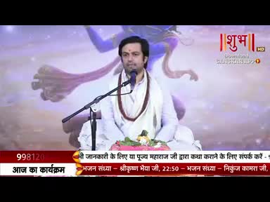 A man in white robes sits on a stage, speaking into a microphone. The Shubh TV logo is visible, and a scrolling text bar runs along the bottom of the screen.
