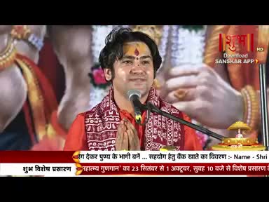 A man in a red shirt and patterned scarf speaks into a microphone, his hands clasped in front of him. The logo for Shubh TV is visible in the corner, along with text in Hindi.
